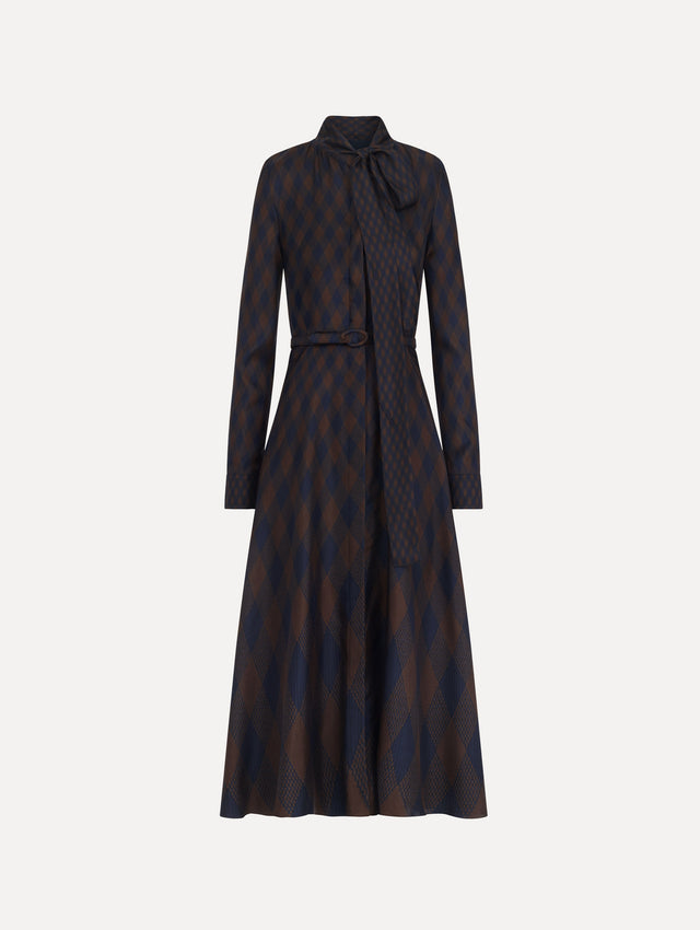 The model is wearing the argyle silk twill tie neck dress with long sleeves, a tie neckline, and an argyle print in navy and brown.