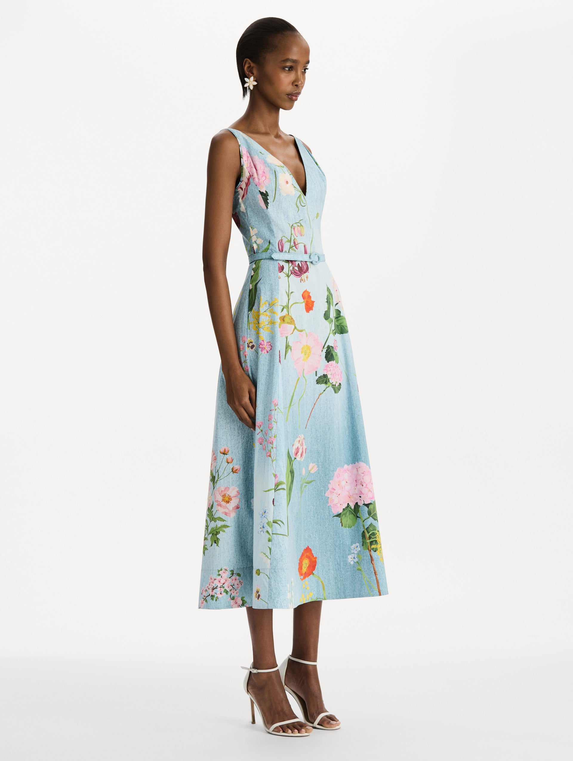 The model is wearing the mixed botanical cotton poplin dress with a sleeveless V-neck silhouette and an all-over floral print in blue multi. Side view. 