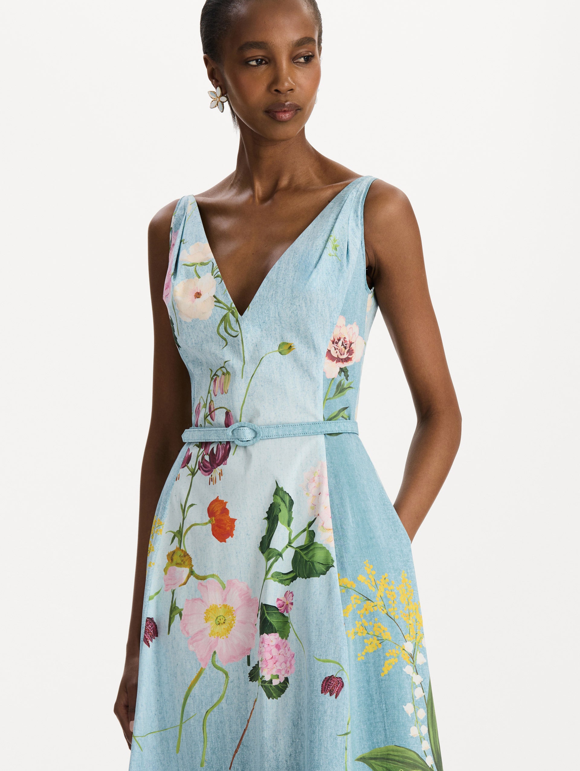 The model is wearing the mixed botanical cotton poplin dress with a sleeveless V-neck silhouette and an all-over floral print in blue multi. Zoom view. 