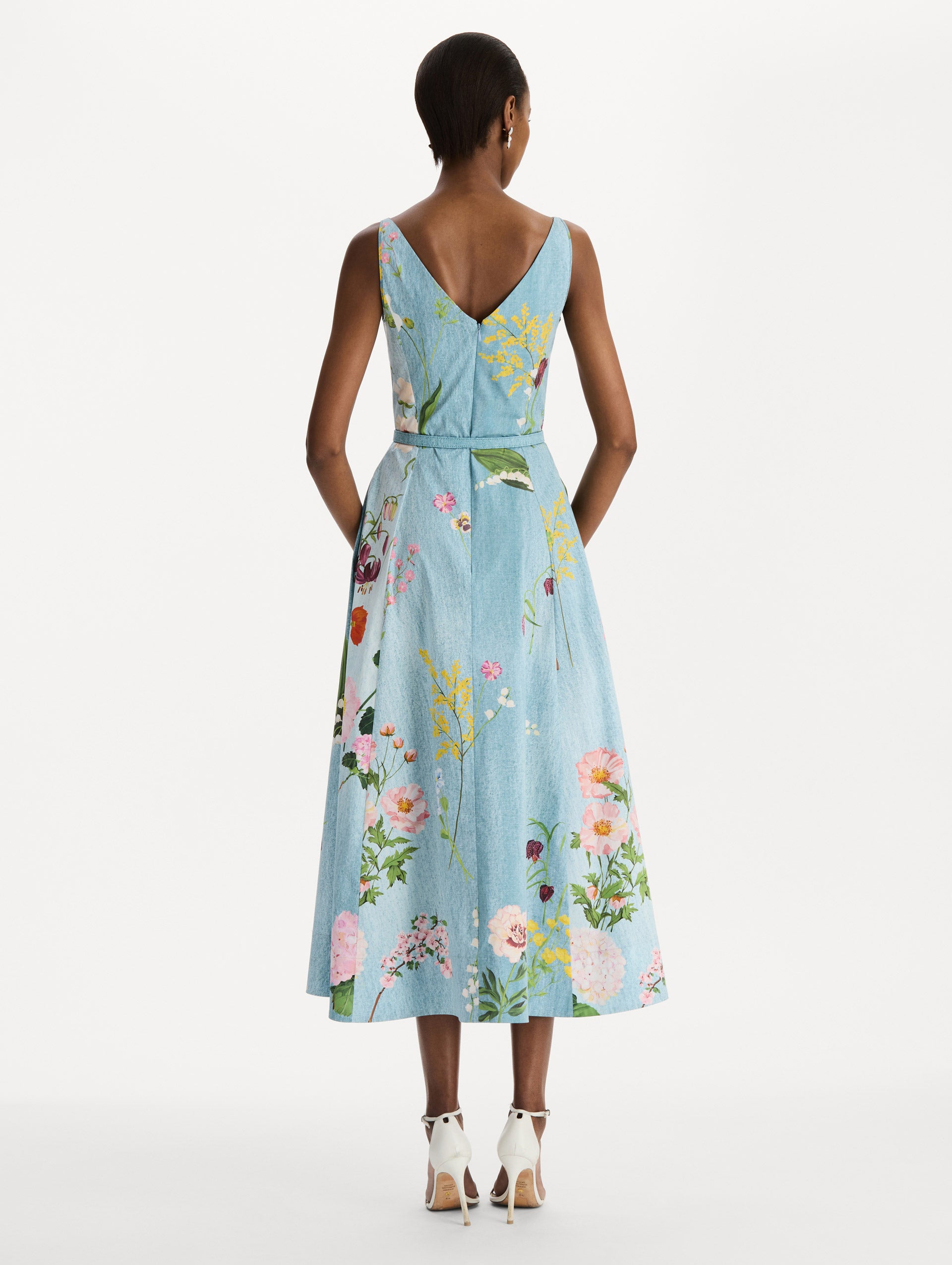 The model is wearing the mixed botanical cotton poplin dress with a sleeveless V-neck silhouette and an all-over floral print in blue multi.