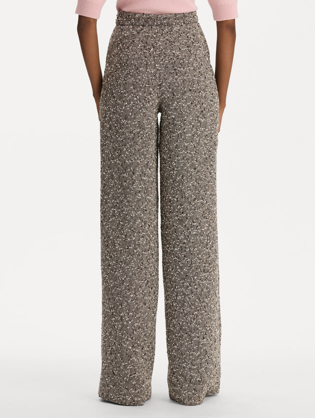 The model is wearing the slubby wool tweed gauze pant with a tailored silhouette in an ivory and brown palette. Back view. 