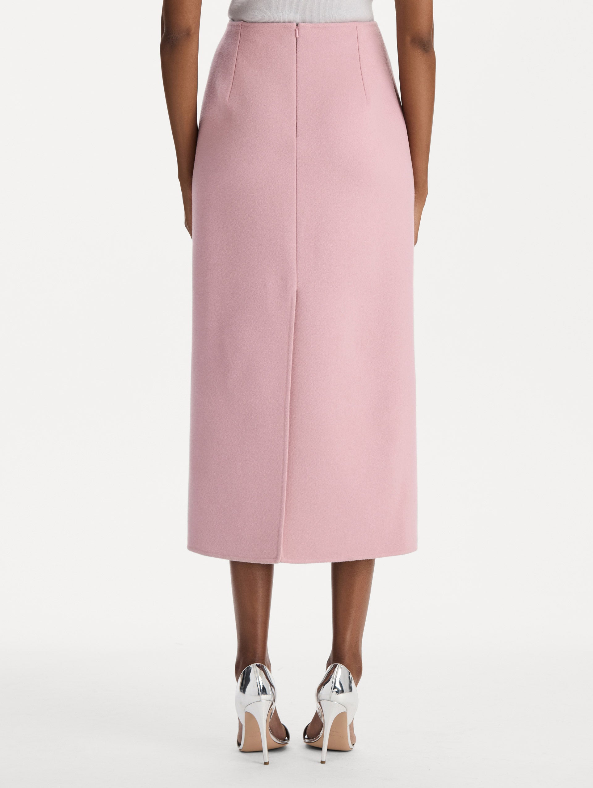 The model is wearing the wool pencil skirt with a structured silhouette in the color blush. Back view. 