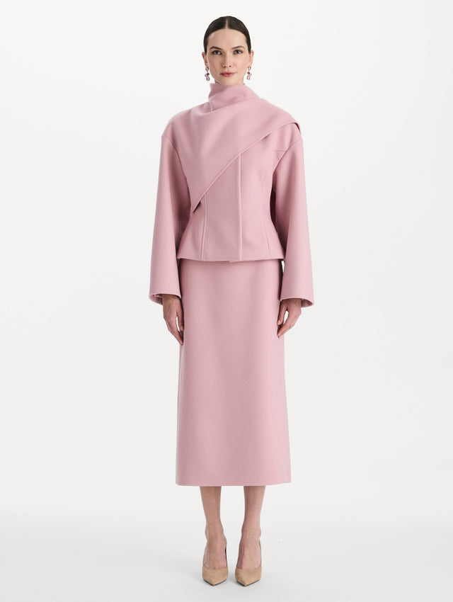 The model is wearing the drape-detailed wool coat with long sleeves in the color blush. Front view. 