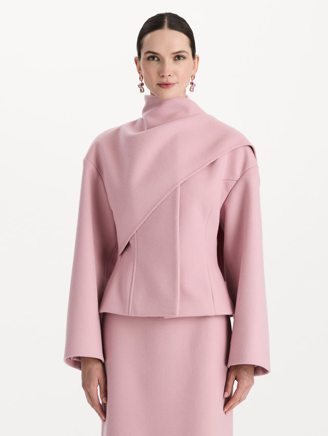 The model is wearing the drape-detailed wool coat with long sleeves in the color blush. Front view. 