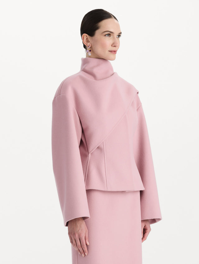 The model is wearing the drape-detailed wool coat with long sleeves in the color blush. Side view. 