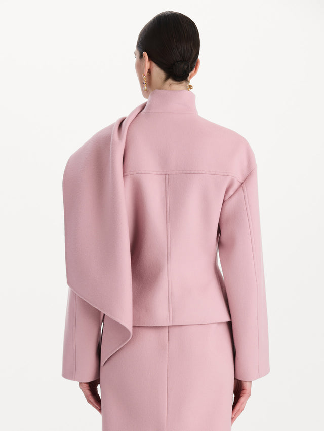 The model is wearing the drape-detailed wool coat with long sleeves in the color blush. Back view. 