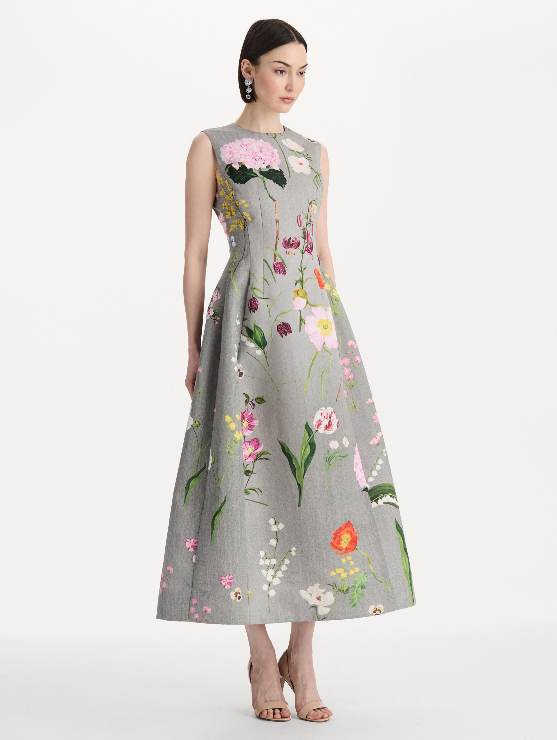 The model is wearing the mixed botanical faille cocktail dress with a sleeveless silhouette in the color grey multi. Side view. 