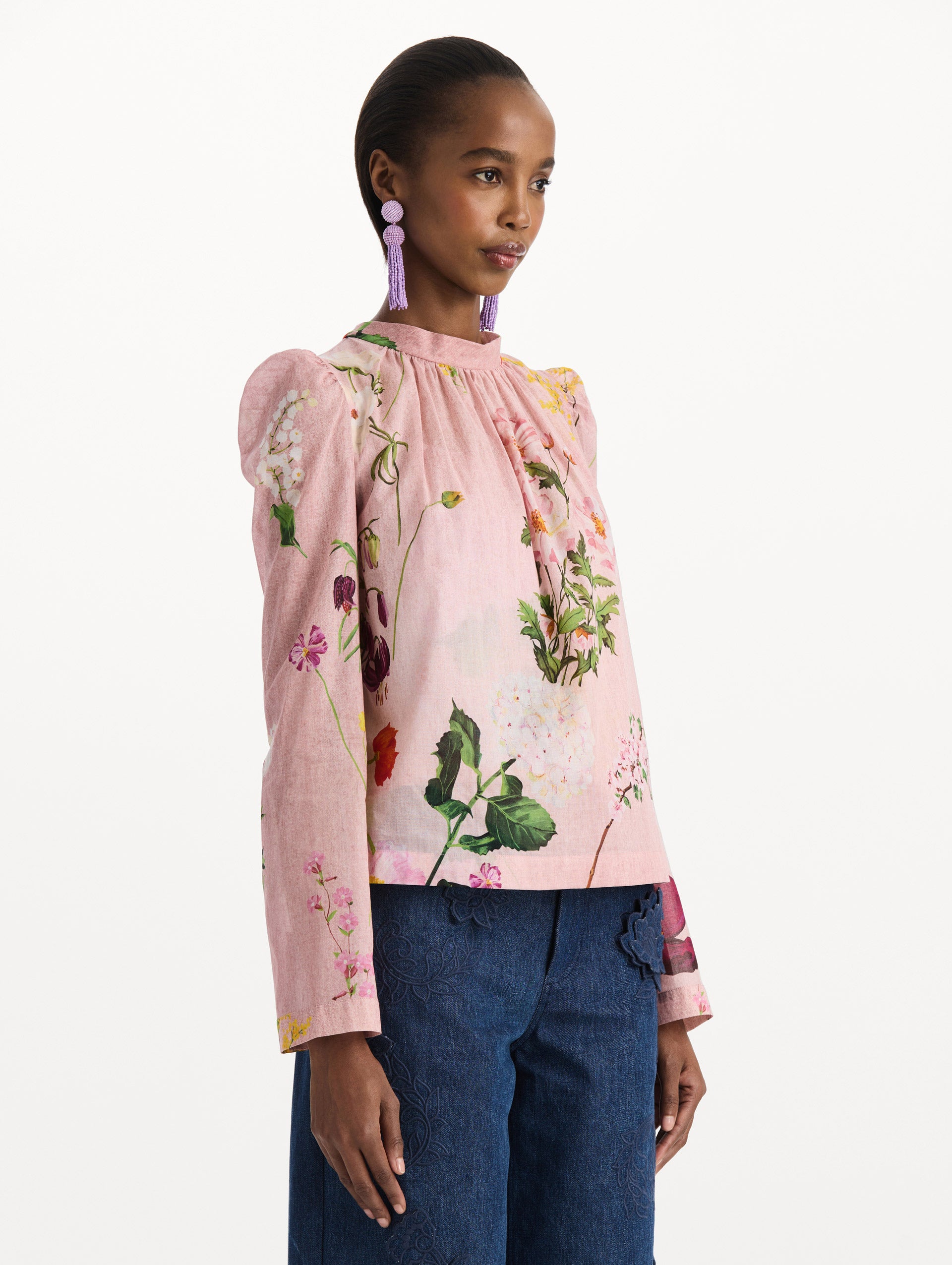 The model is wearing the mixed botanical tie-detailed blouse with a tie neckline and an all-over floral print in a blush multi palette. Side view. 