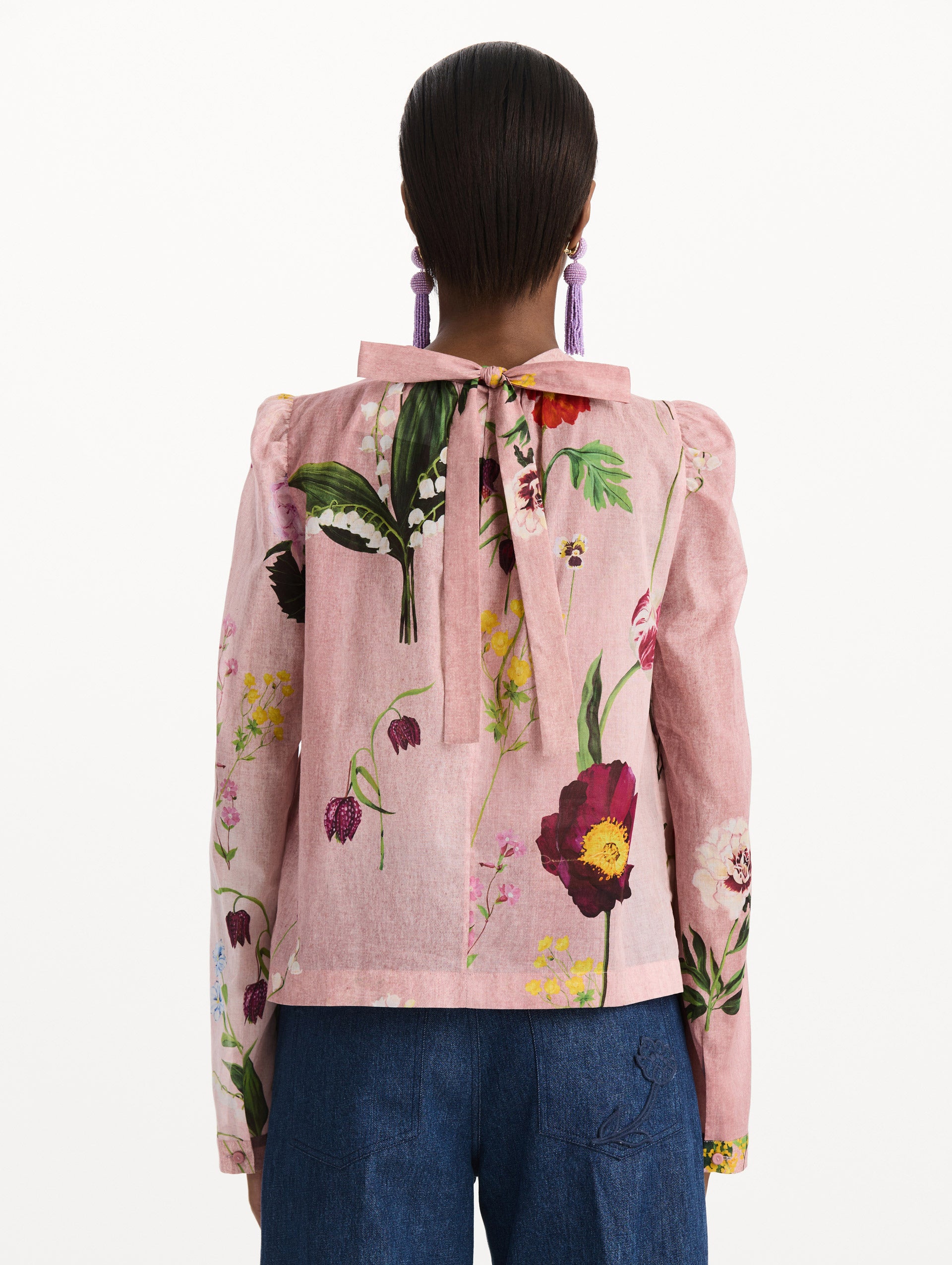 The model is wearing the mixed botanical tie-detailed blouse with a tie neckline and an all-over floral print in a blush multi palette. Back view. 