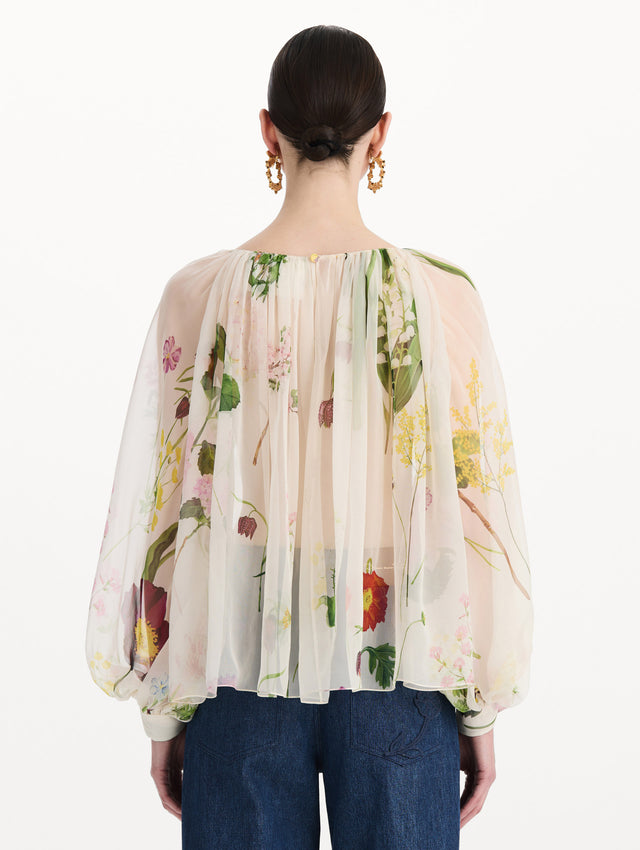 The model is wearing the mixed botanical silk chiffon blouse with long sleeves and an all-over floral print in ecru tones. Back view. 