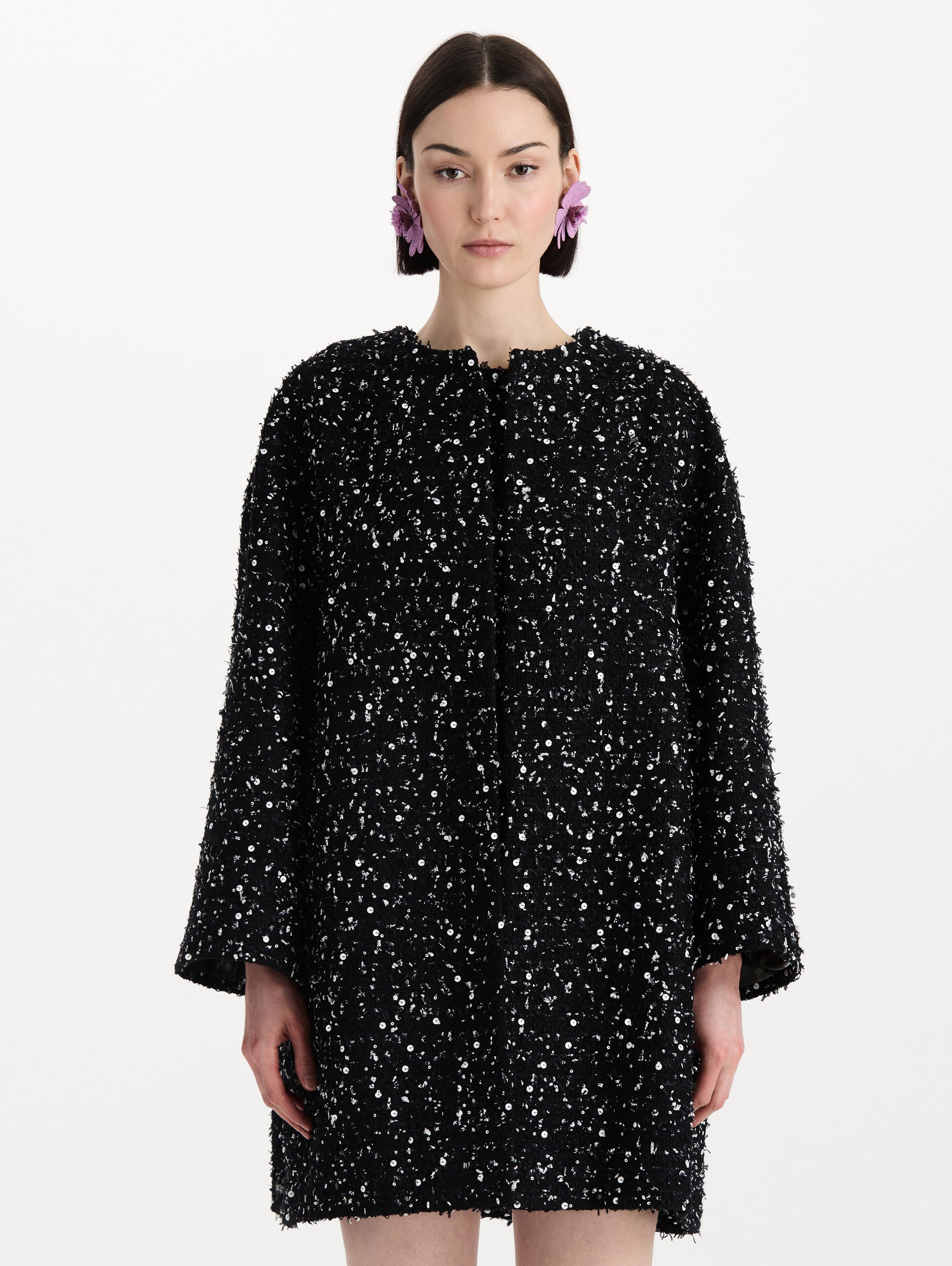 The model is wearing the sequin ribbon tweed coat with a black and white tweed finish and a tailored silhouette. Front view. 