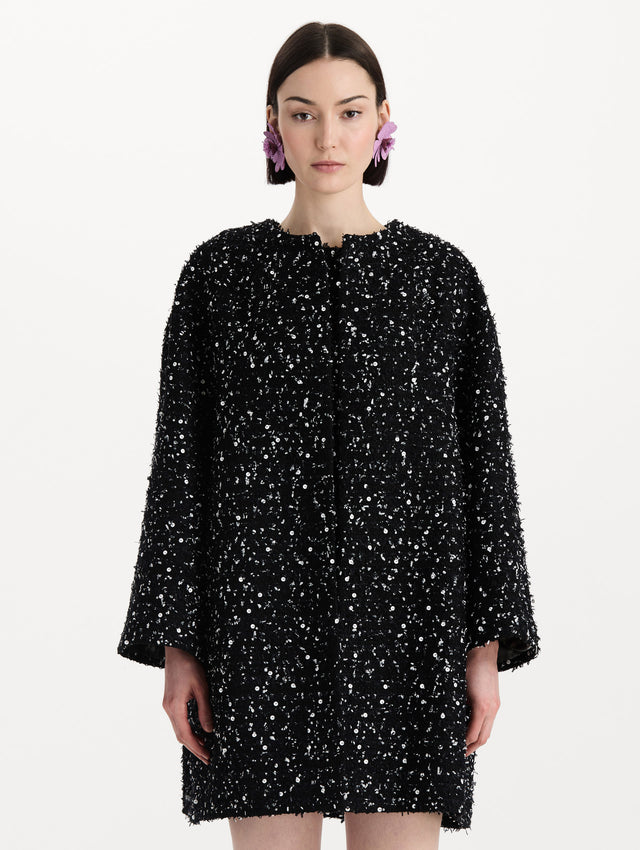 The model is wearing the sequin ribbon tweed coat with a black and white tweed finish and a tailored silhouette. Front view. 