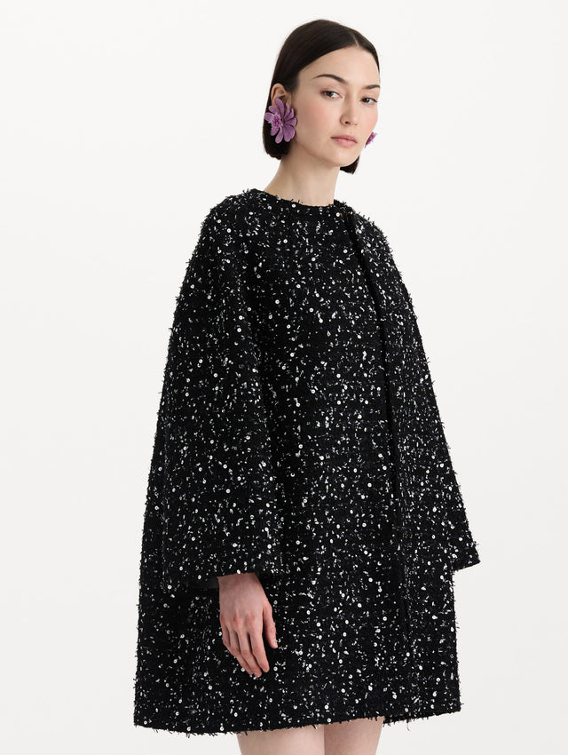 The model is wearing the sequin ribbon tweed coat with a black and white tweed finish and a tailored silhouette. Side view. 