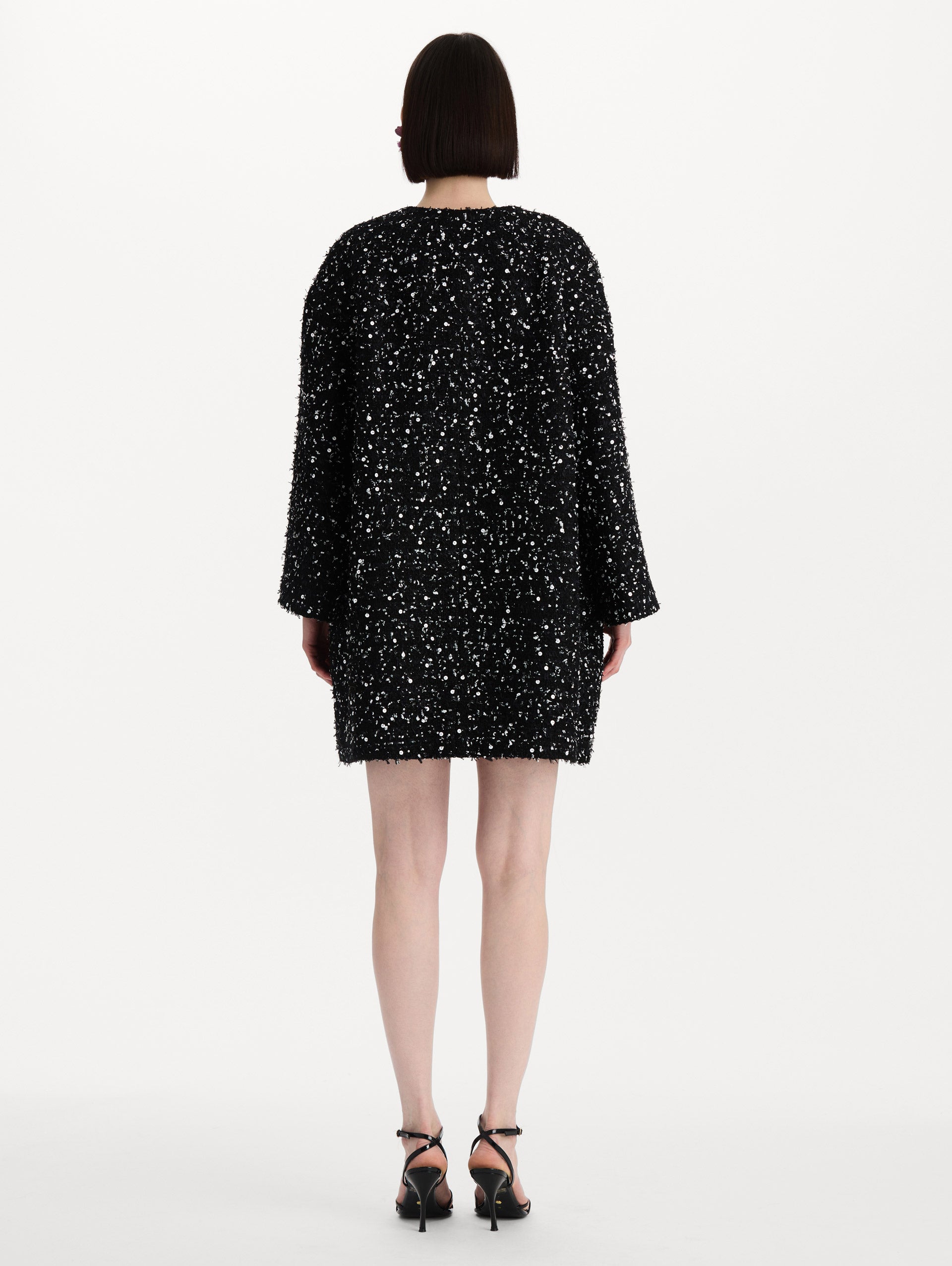 The model is wearing the sequin ribbon tweed coat with a black and white tweed finish and a tailored silhouette. Back view. 