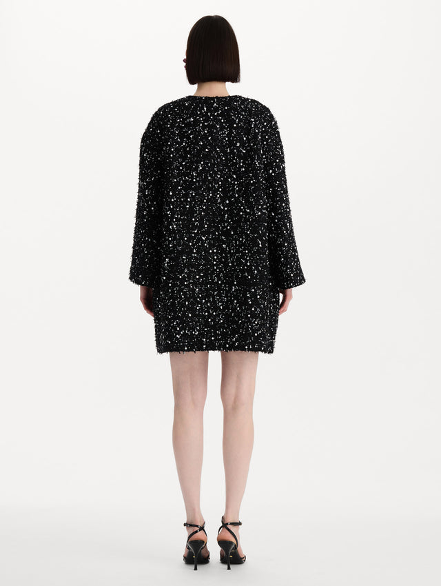 The model is wearing the sequin ribbon tweed coat with a black and white tweed finish and a tailored silhouette. Back view. 