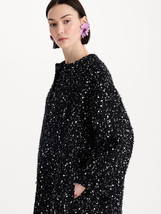 The model is wearing the sequin ribbon tweed coat with a black and white tweed finish and a tailored silhouette. Zoom view. 