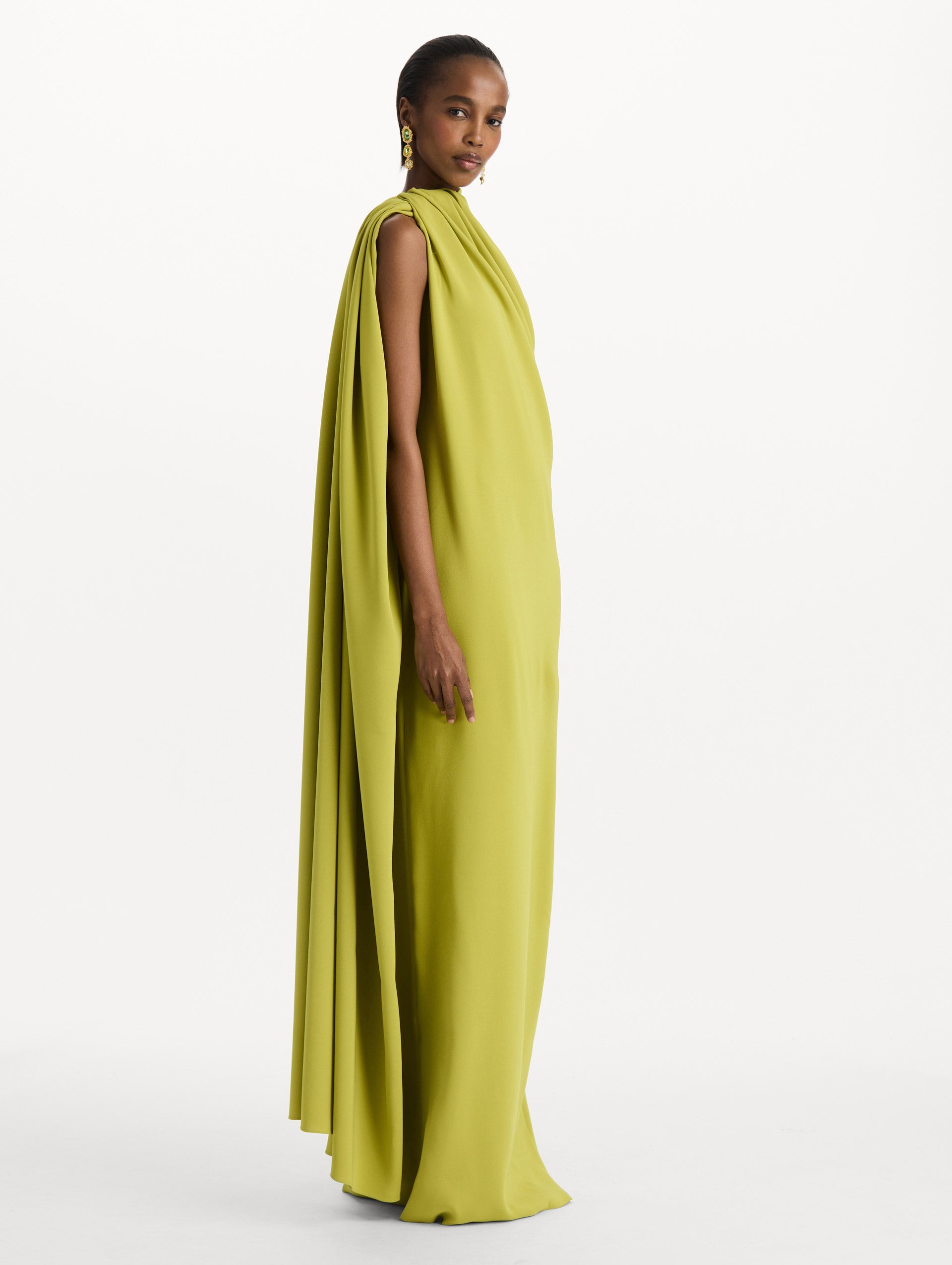 The model is wearing the drape-detailed georgette caftan with a halter neckline in the color peridot. Side view. 