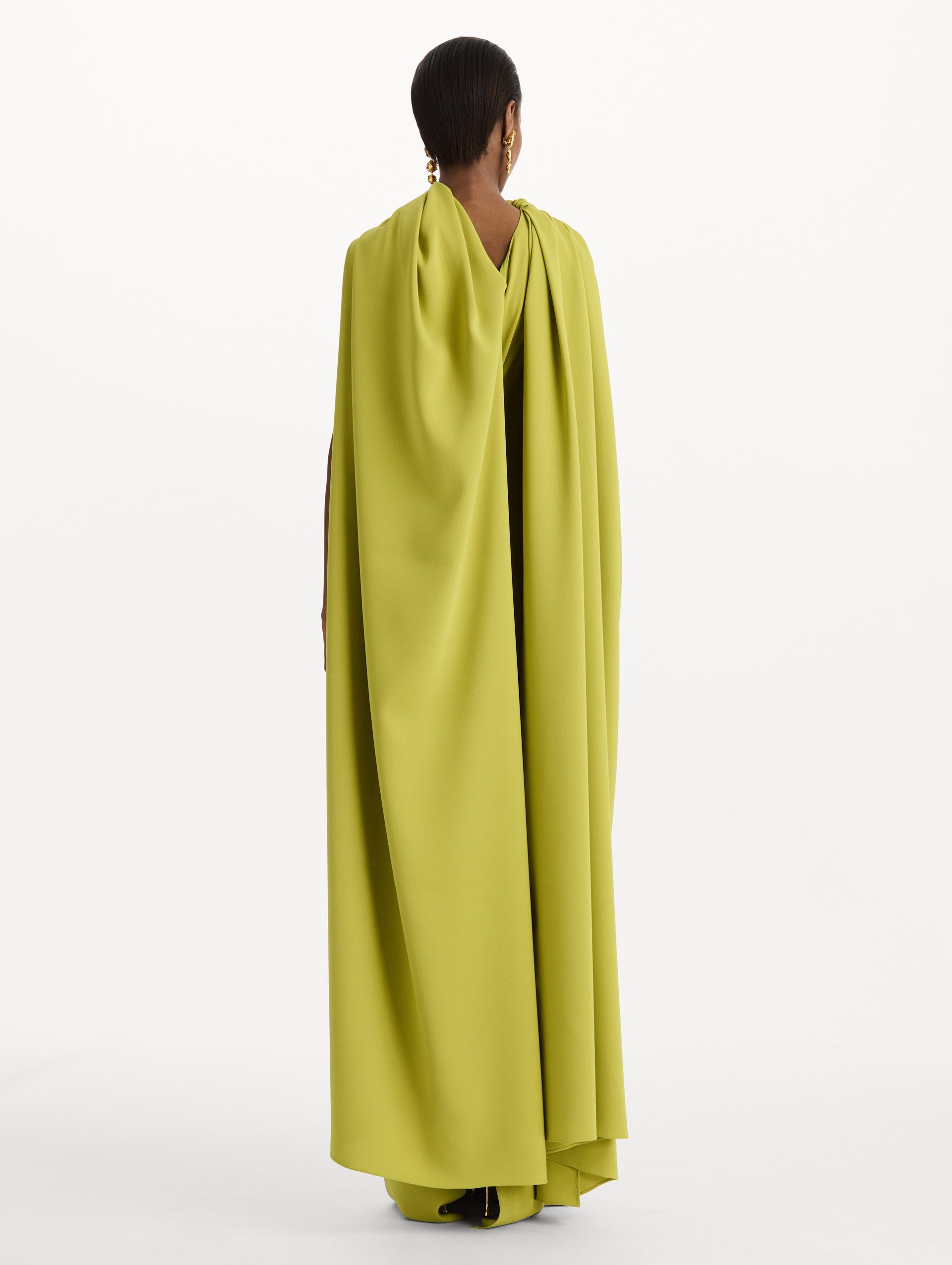 The model is wearing the drape-detailed georgette caftan with a halter neckline in the color peridot. Back view. 
