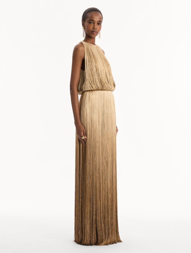 The model is wearing the Ombré Fringe Sleeveless Gown. Featuring layers of ombré fringe, a softly draped bodice, and elongated skirt. Side View.