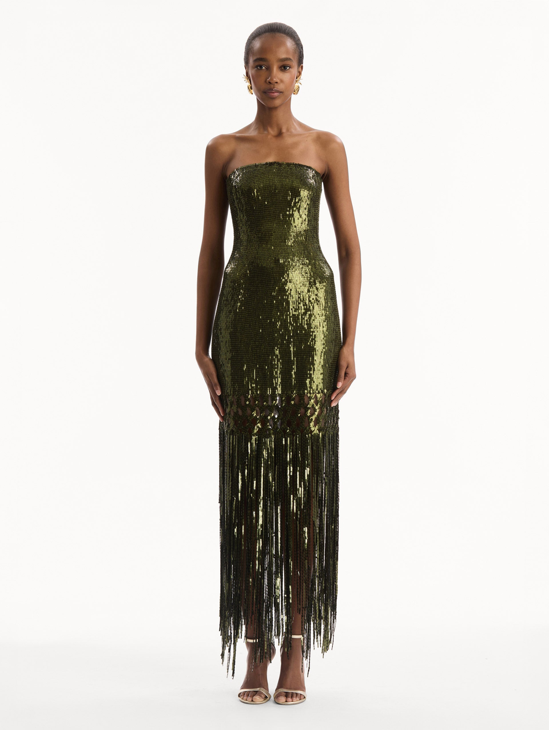 The model is wearing the Sequin Fringe Gown in green. Featuring a strapless neckline, fitted silhouette, and an open lattice detail cascading into a fringe skirt. Front View.