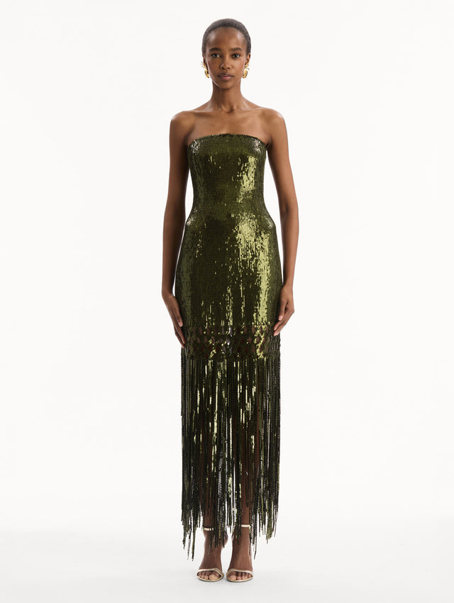 The model is wearing the Sequin Fringe Gown in green. Featuring a strapless neckline, fitted silhouette, and an open lattice detail cascading into a fringe skirt. Front View.