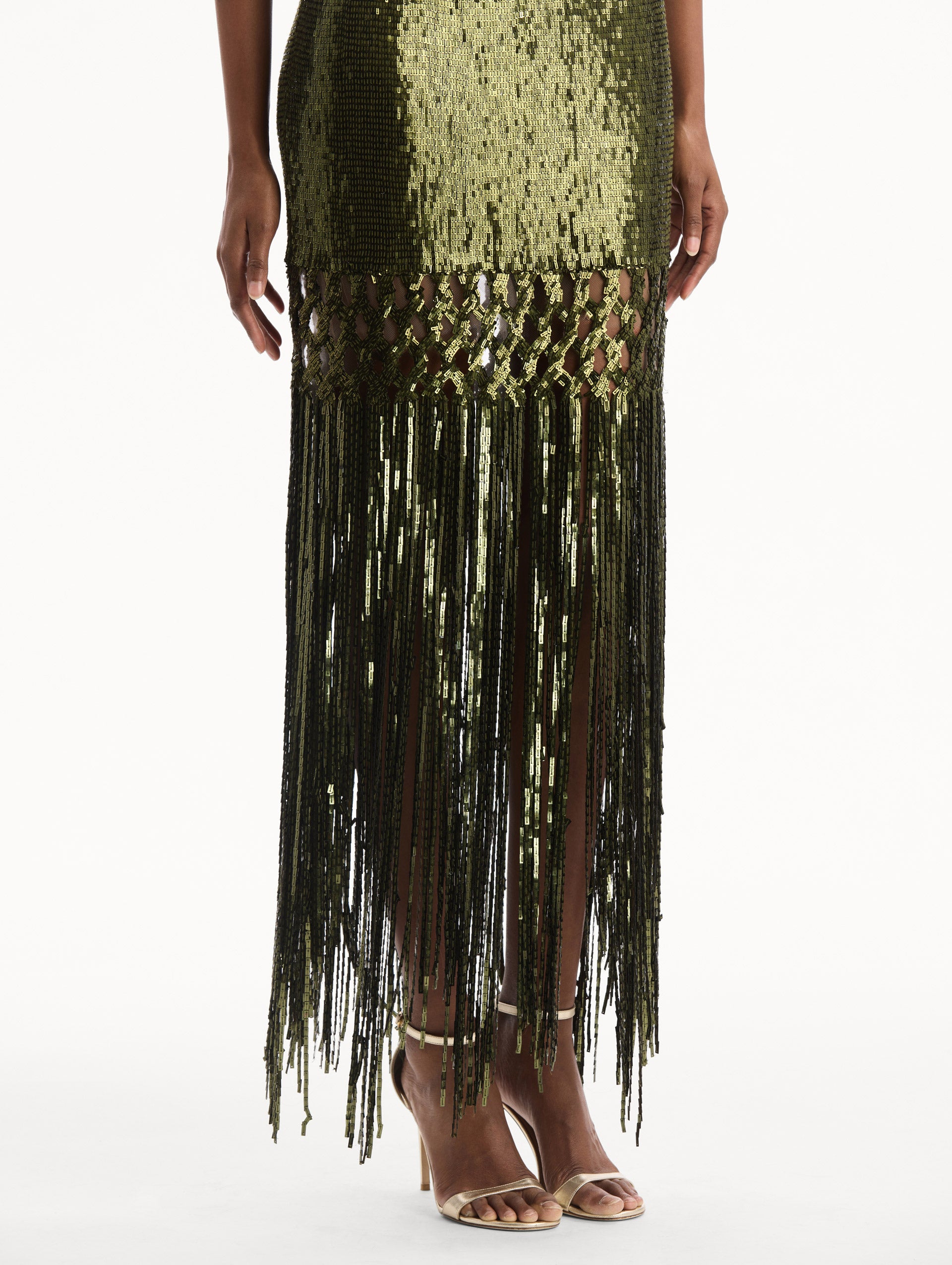 The model is wearing the Sequin Fringe Gown in green. Featuring a strapless neckline, fitted silhouette, and an open lattice detail cascading into a fringe skirt. Detail View.