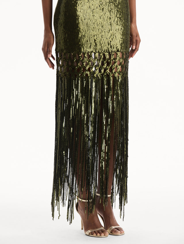 The model is wearing the Sequin Fringe Gown in green. Featuring a strapless neckline, fitted silhouette, and an open lattice detail cascading into a fringe skirt. Detail View.