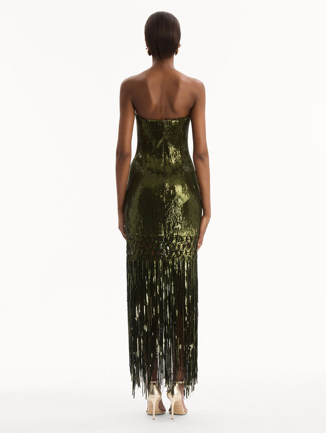 The model is wearing the Sequin Fringe Gown in green. Featuring a strapless neckline, fitted silhouette, and an open lattice detail cascading into a fringe skirt. Back View.