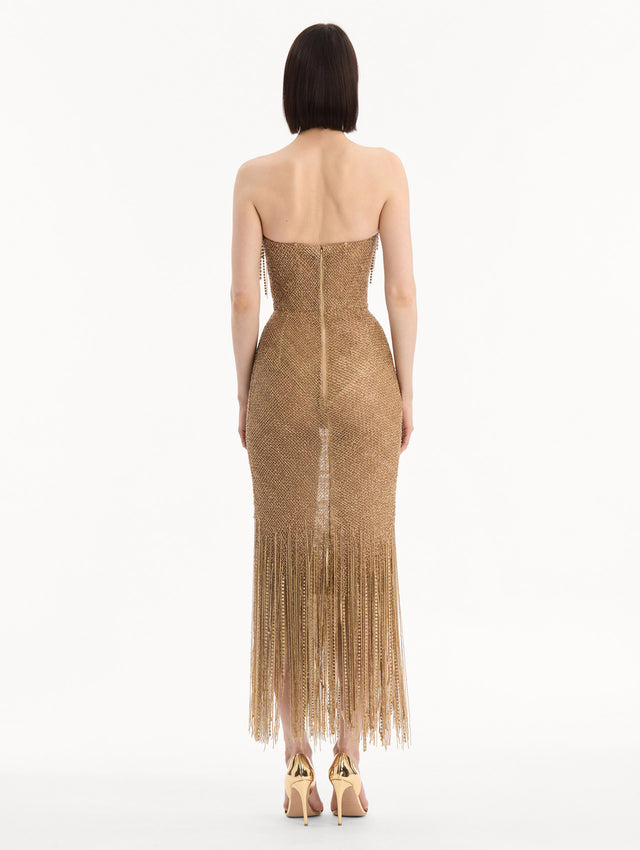 The model is wearing the Bugle Bead & Crystal Fringe Gown in Gold. Featuring a strapless neckline, layers of bugle beads and crystals draped across, and a fringe skirt. Back View.
