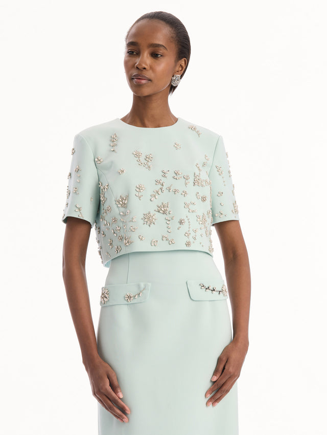 The model is wearing the Crystal Floral Embroidered Gown in Saltwater Blue. Featuring a strapless neckline, faux front flap pockets with crystal embroidery, and a long, column silhouette. Detail View.