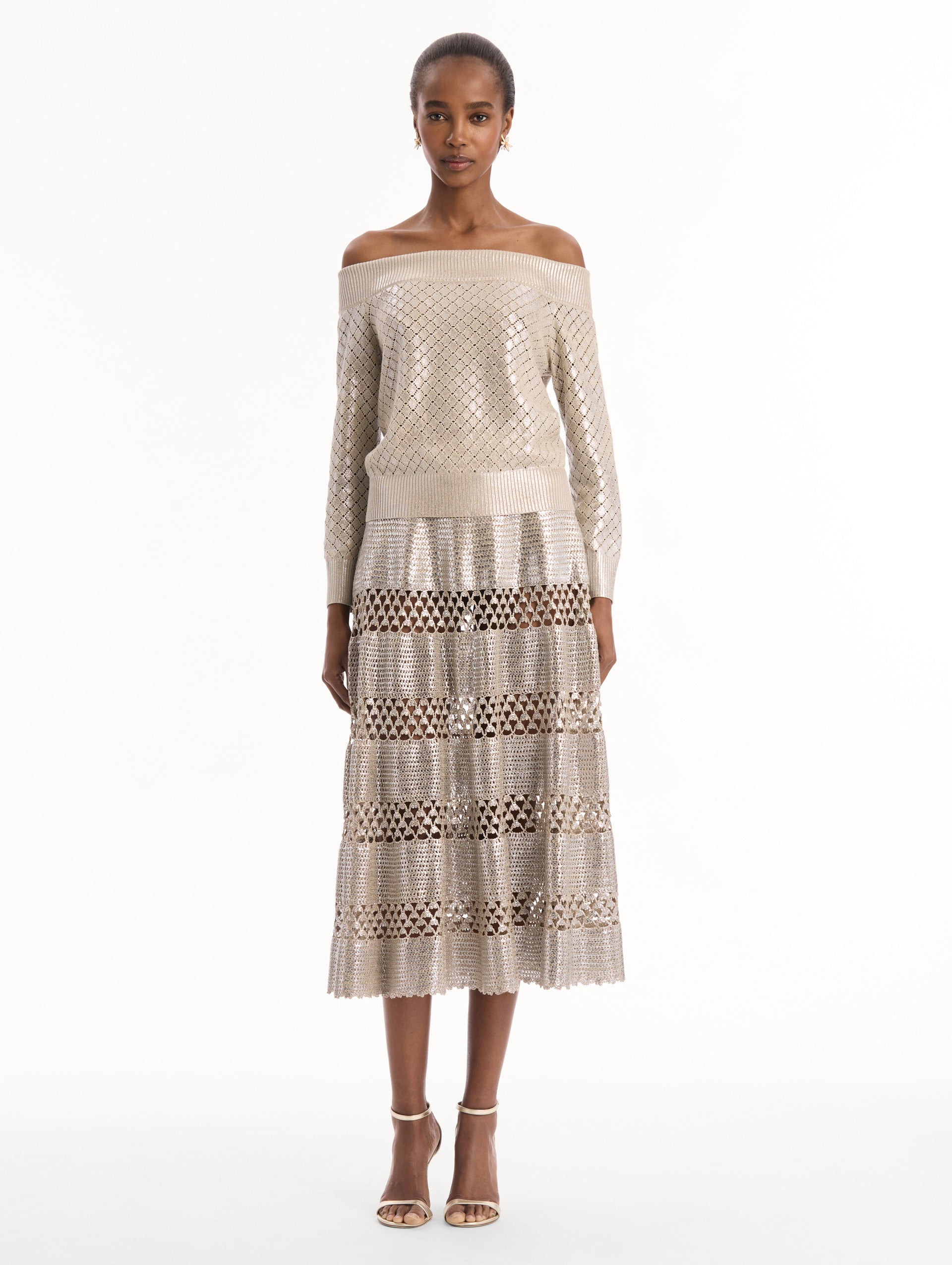 The model is wearing the Silver Foil Off-Shoulder Pullover. Featuring a lattice knit pattern, off-the-shoulder neckline, long sleeves, and ribbed trims. Front View.