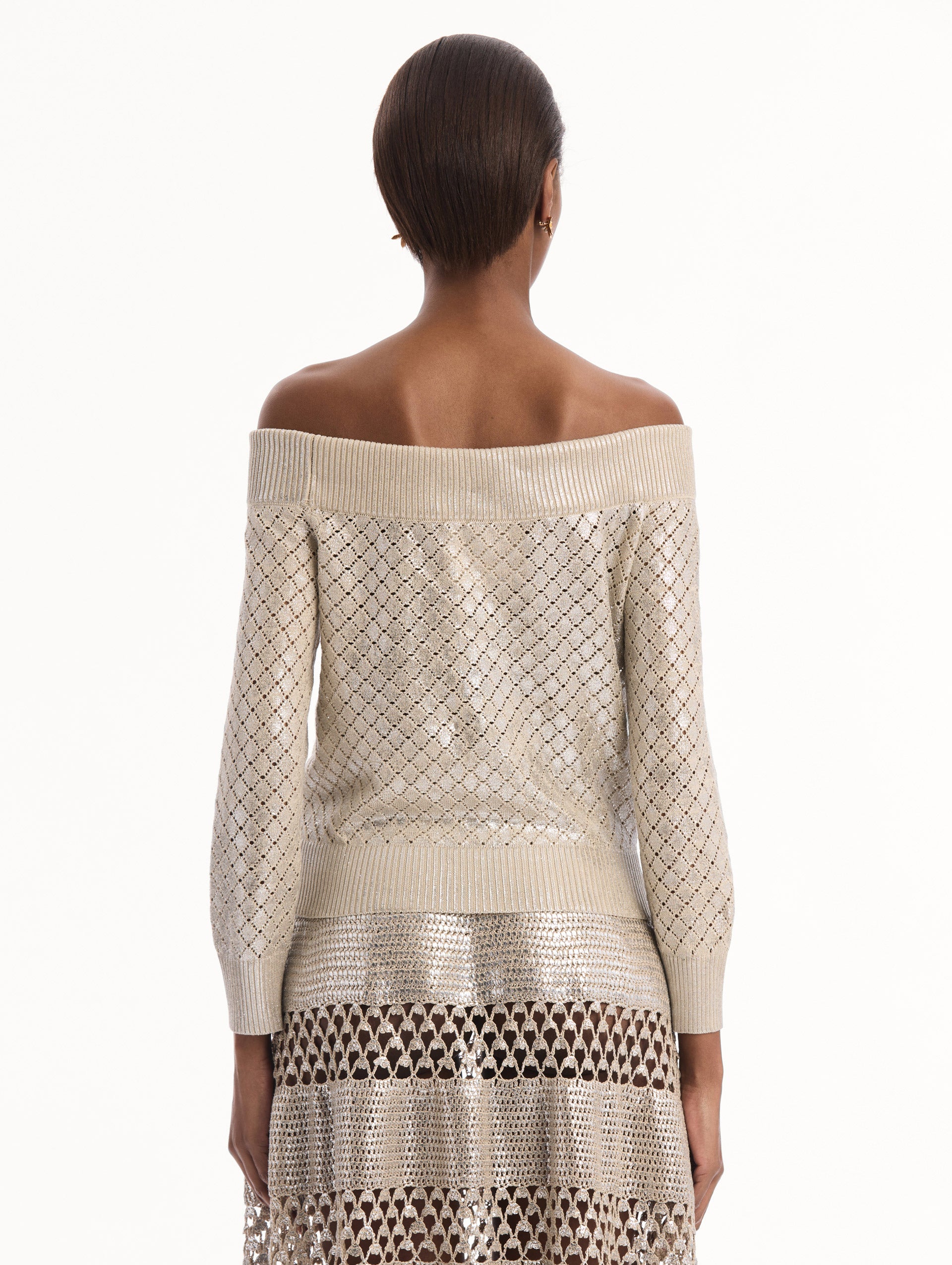 The model is wearing the Silver Foil Off-Shoulder Pullover. Featuring a lattice knit pattern, off-the-shoulder neckline, long sleeves, and ribbed trims. Back View.