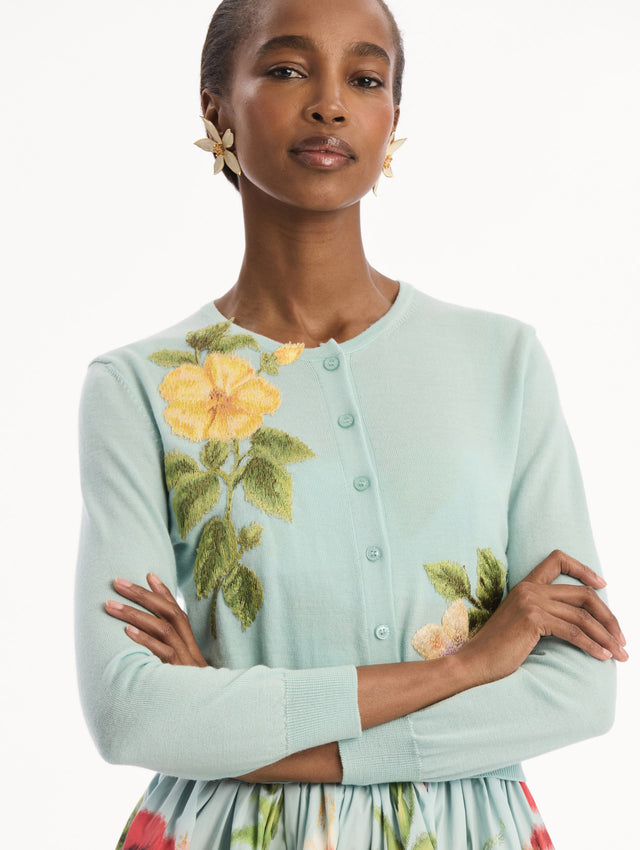 The model is wearing the Chiné Dominican Mixed-Floral Threadwork Cardigan in Saltwater Blue with threaded Dominican florals. Featuring buttons closures down the center, long sleeves, crew neckline, and ribbed trims. Detail View.