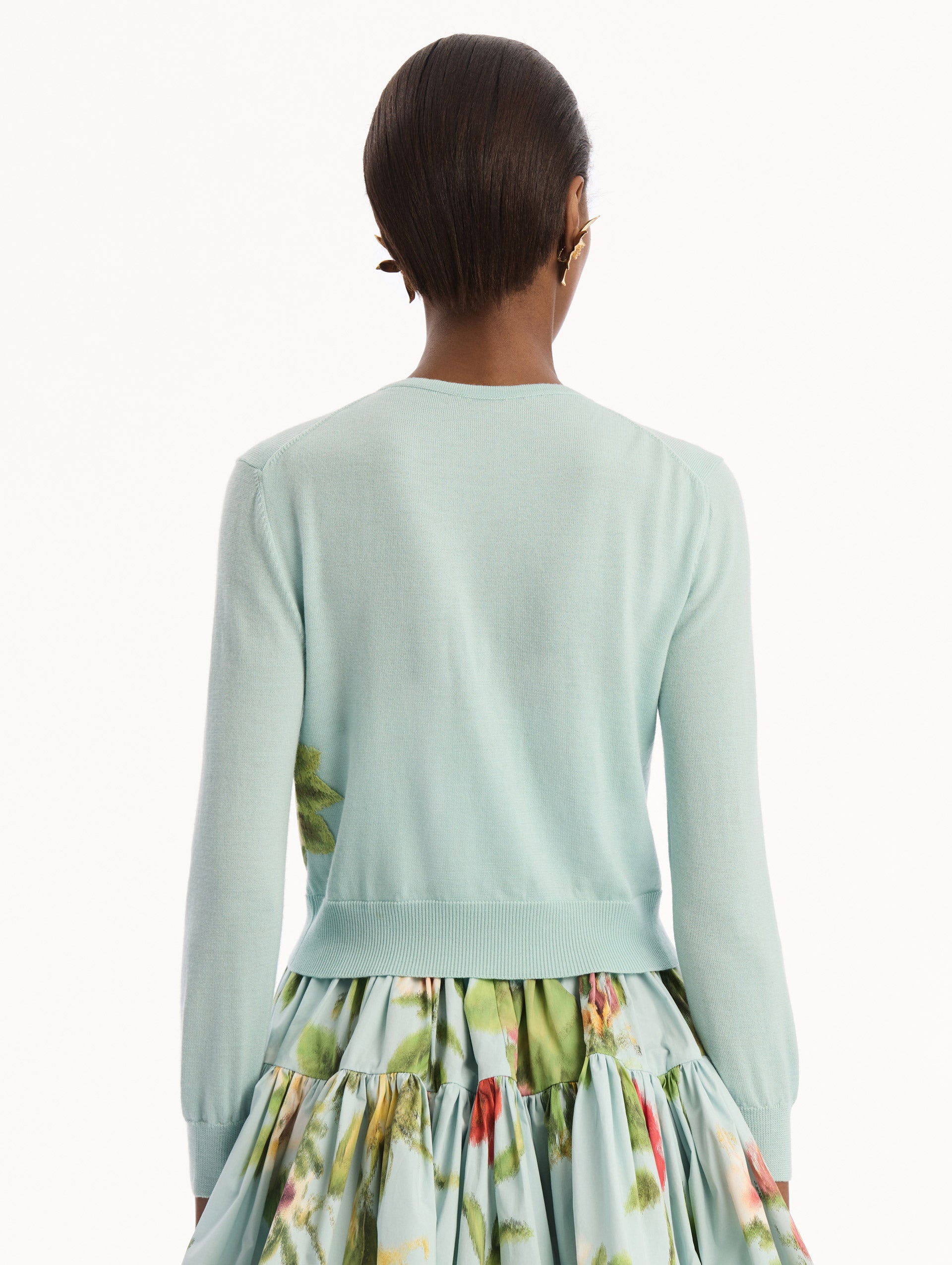 The model is wearing the Chiné Dominican Mixed-Floral Threadwork Cardigan in Saltwater Blue with threaded Dominican florals. Featuring buttons closures down the center, long sleeves, crew neckline, and ribbed trims. Back View.