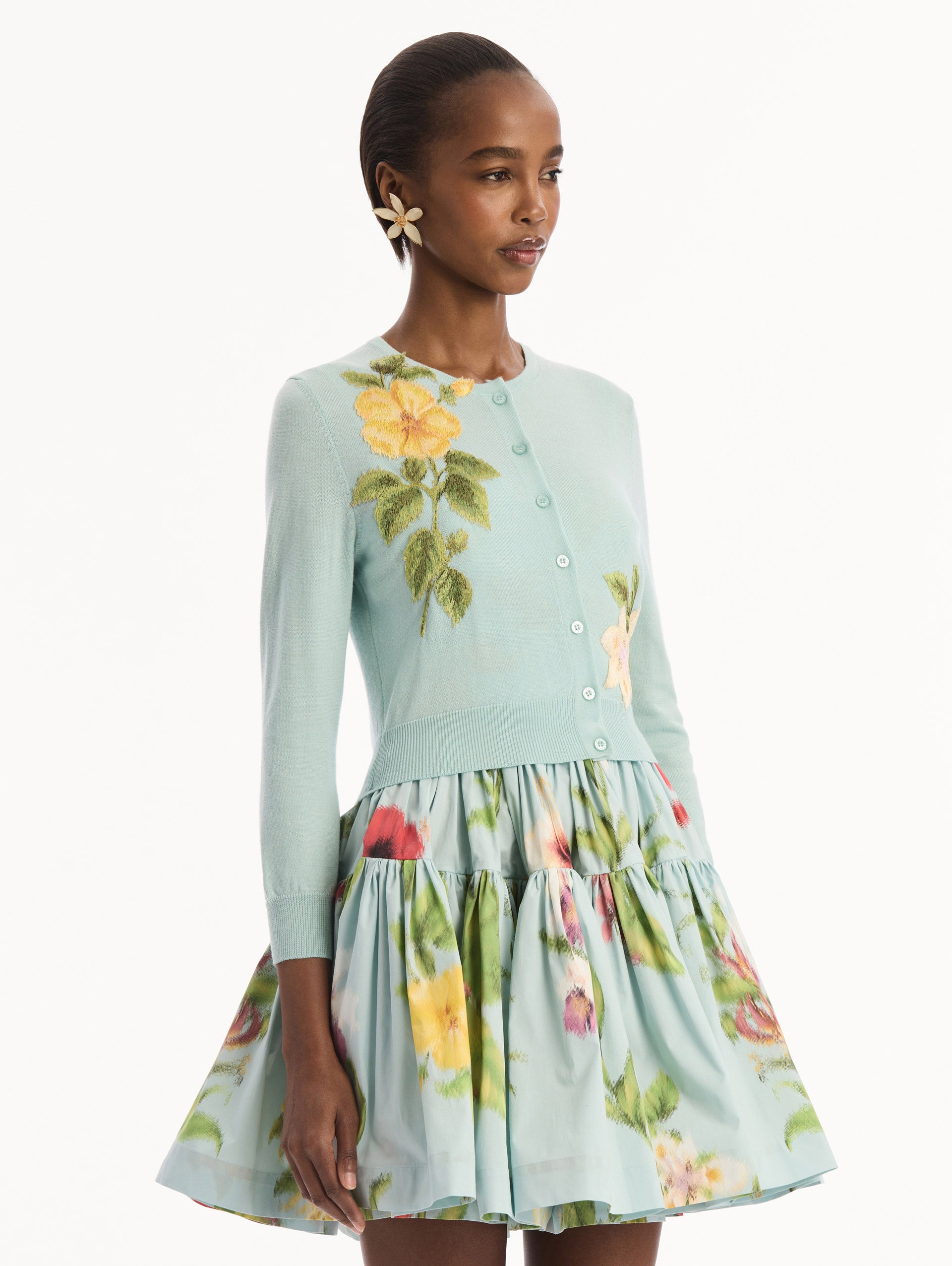 The model is wearing the Chiné Dominican Mixed-Floral Threadwork Cardigan in Saltwater Blue with threaded Dominican florals. Featuring buttons closures down the center, long sleeves, crew neckline, and ribbed trims. Side View.