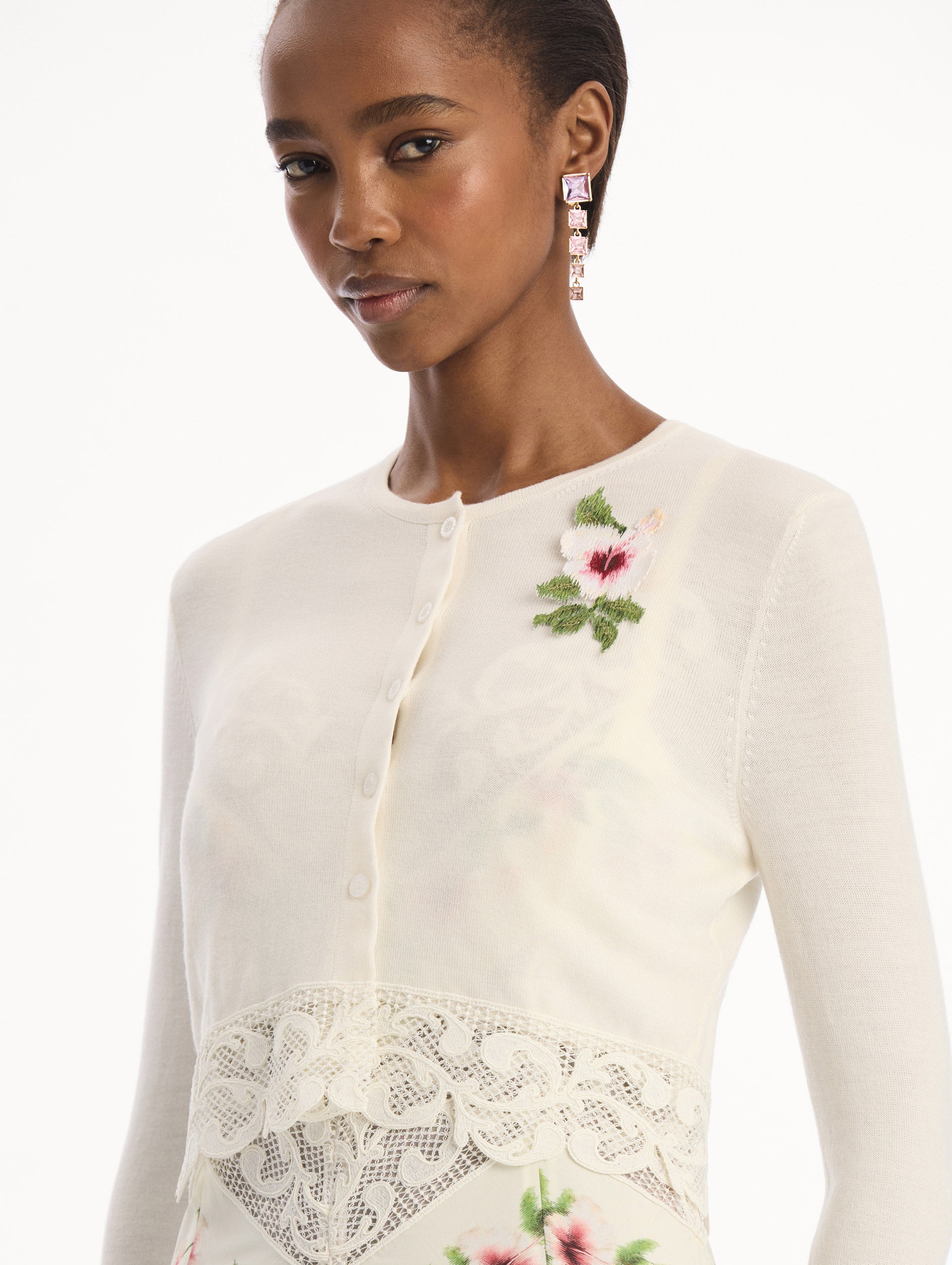 The model is wearing the Chiné Hibiscus Threadwork Cropped Cardigan in Ivory. Featuring a threaded Chiné hibiscus and intricate guipure lace trim. Detail View.