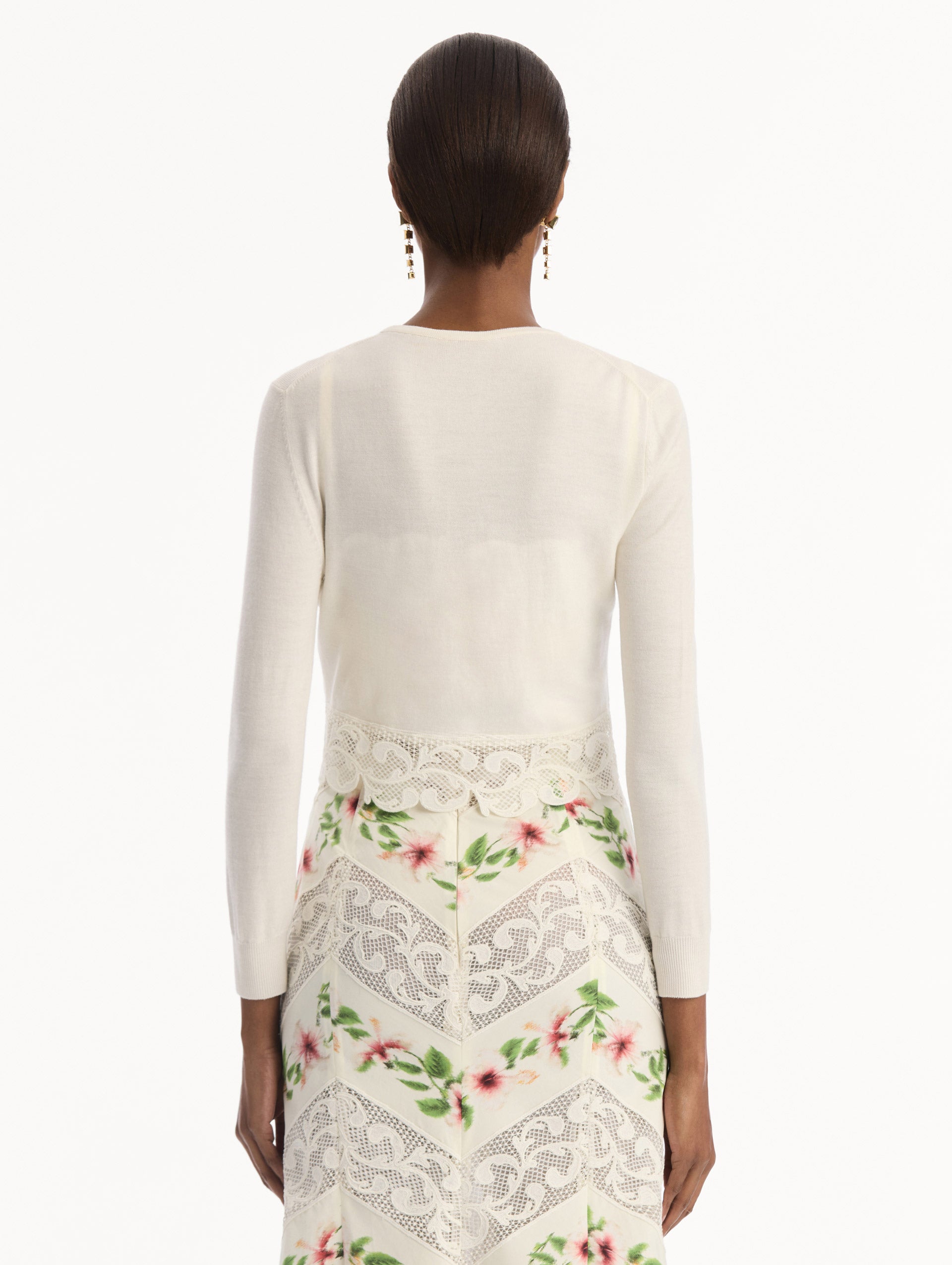 The model is wearing the Chiné Hibiscus Threadwork Cropped Cardigan in Ivory. Featuring a threaded Chiné hibiscus and intricate guipure lace trim. Back View.