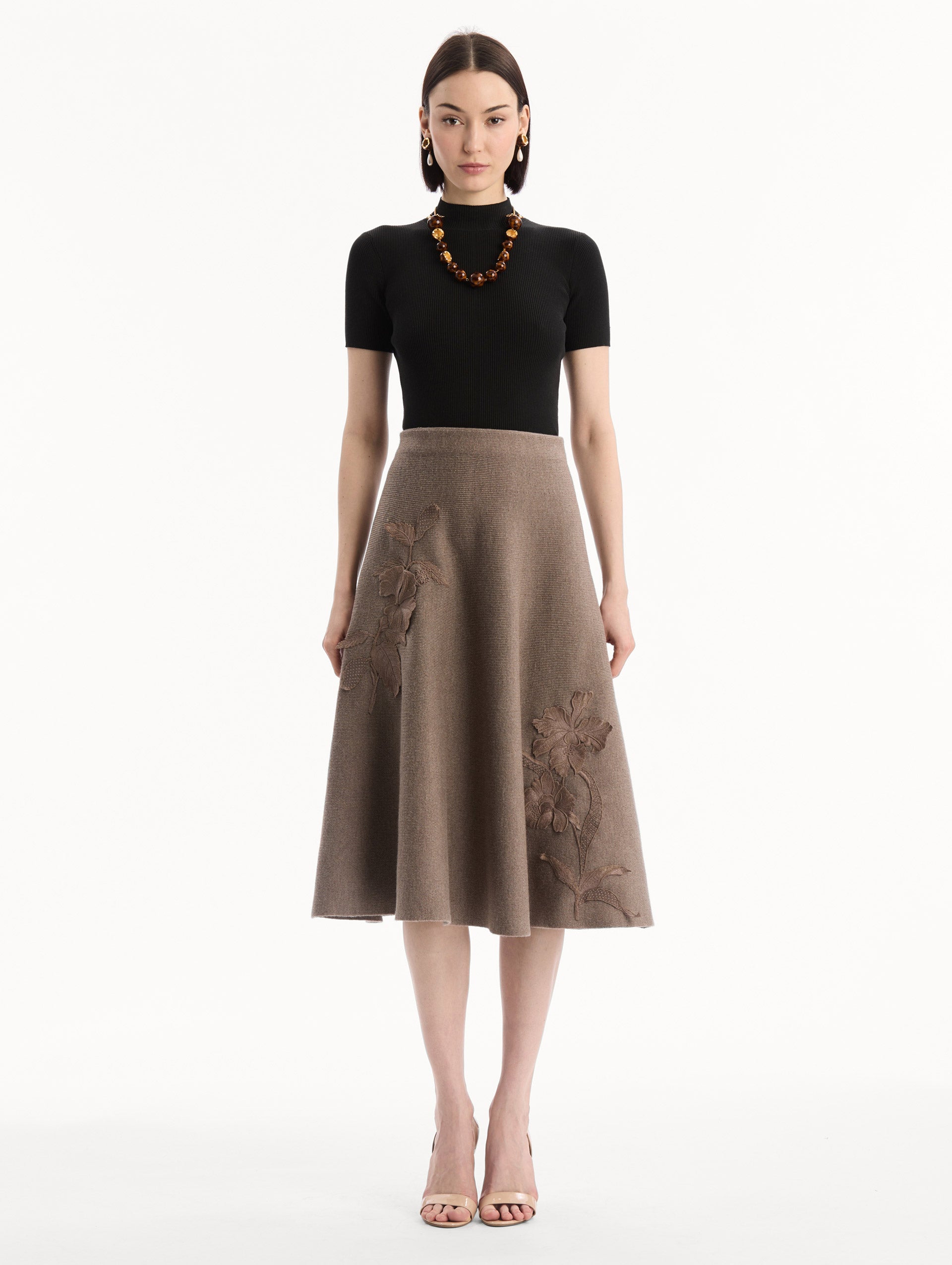 The model is wearing the Hibiscus Embroidered Knit Skirt. Featuring a softly flared silhouette and midi length. Front View.