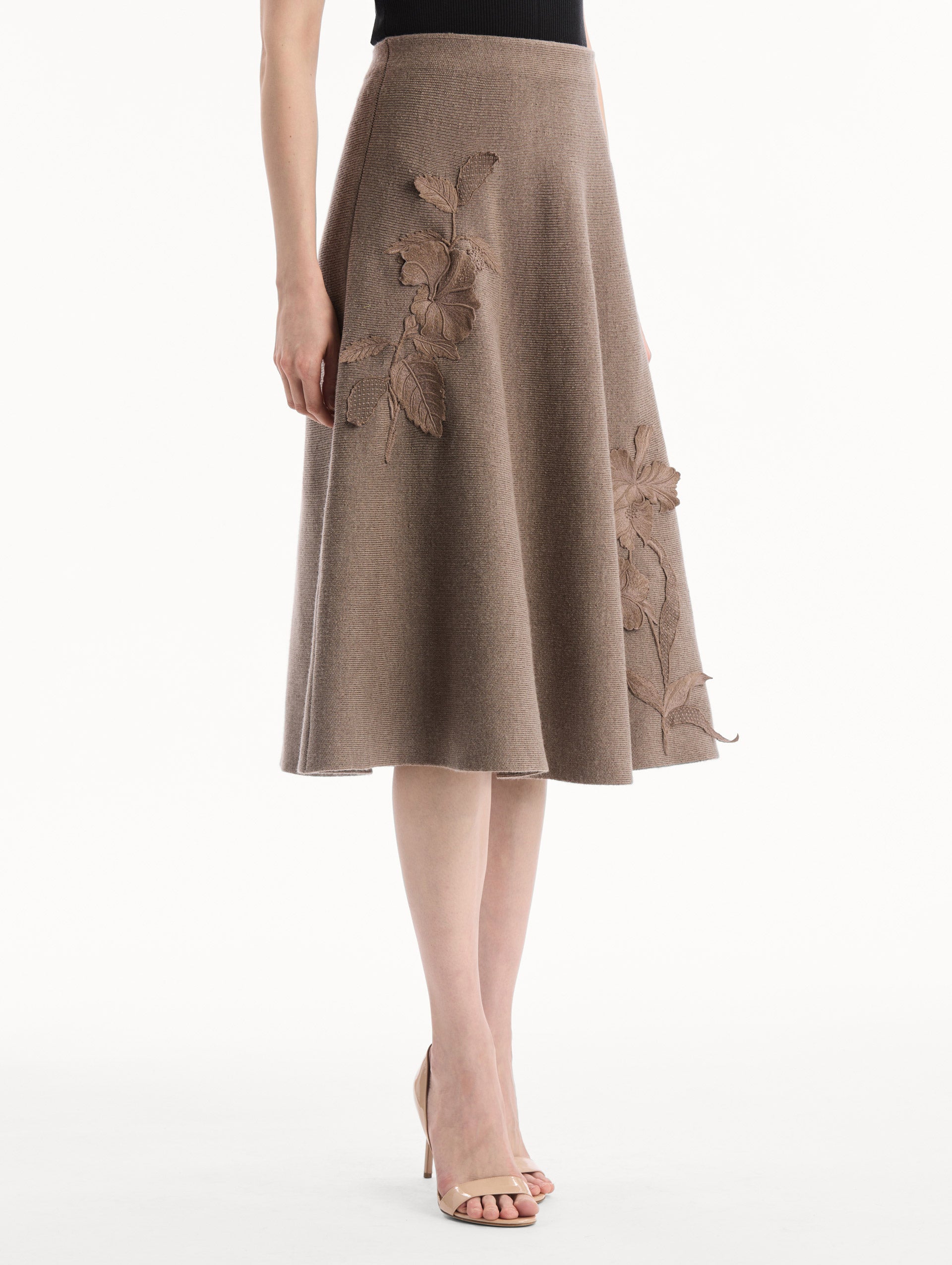 The model is wearing the Hibiscus Embroidered Knit Skirt. Featuring a softly flared silhouette and midi length. Side View.