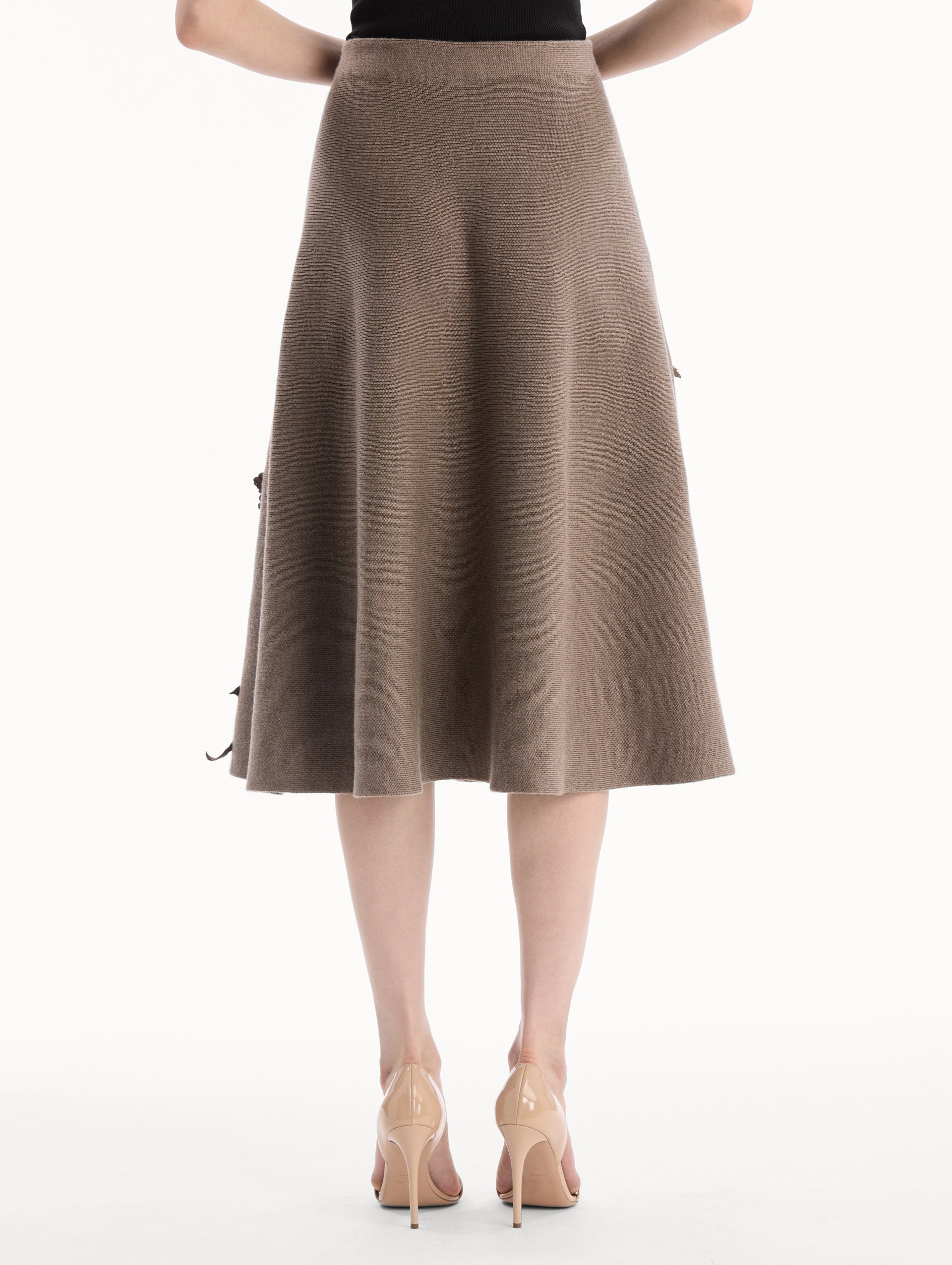 The model is wearing the Hibiscus Embroidered Knit Skirt. Featuring a softly flared silhouette and midi length. Back View.