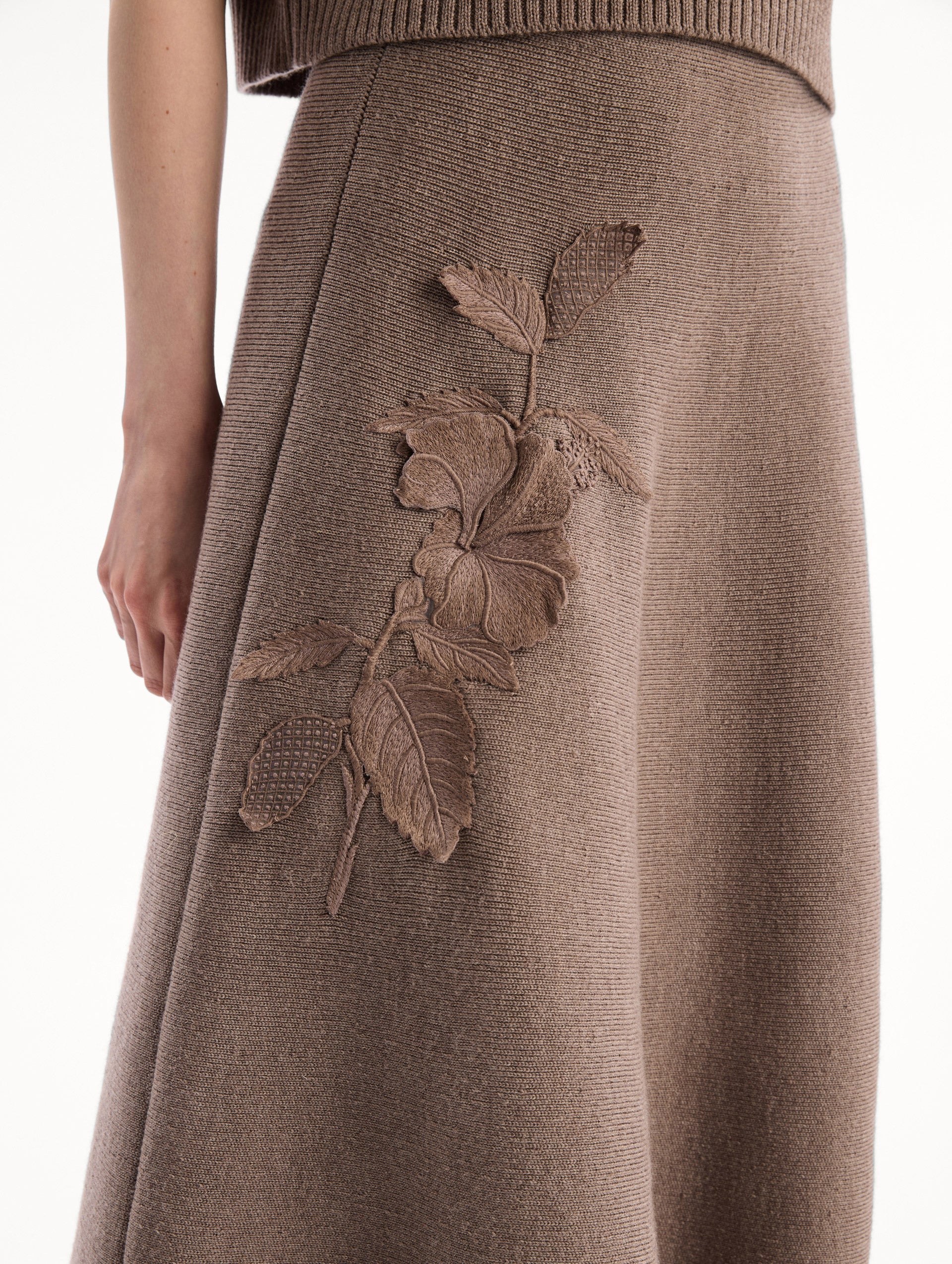 The model is wearing the Hibiscus Embroidered Knit Skirt. Featuring a softly flared silhouette and midi length. Detail View.