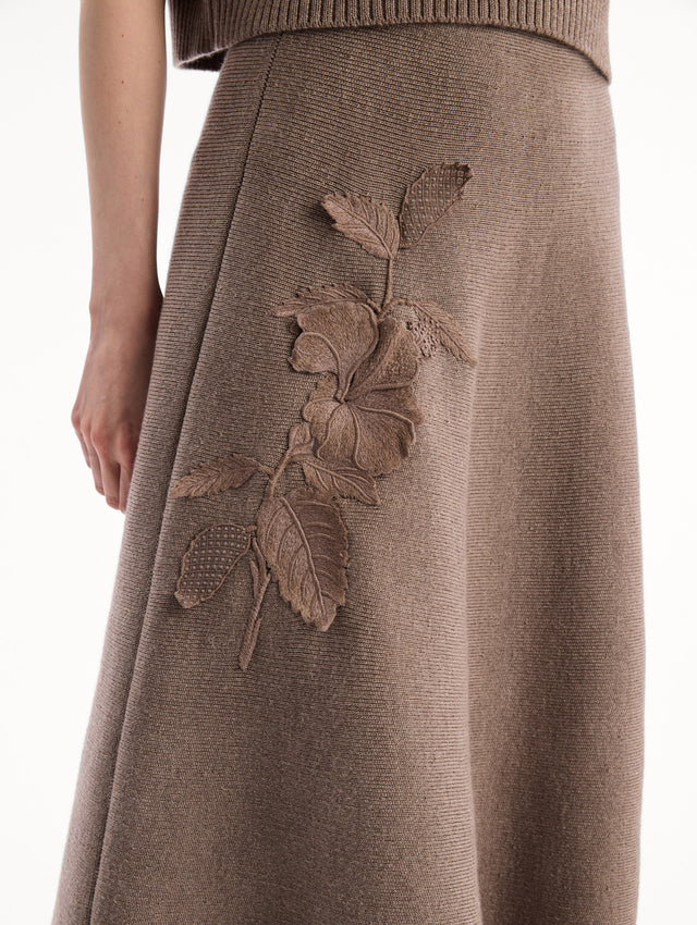 The model is wearing the Hibiscus Embroidered Knit Skirt. Featuring a softly flared silhouette and midi length. Detail View.