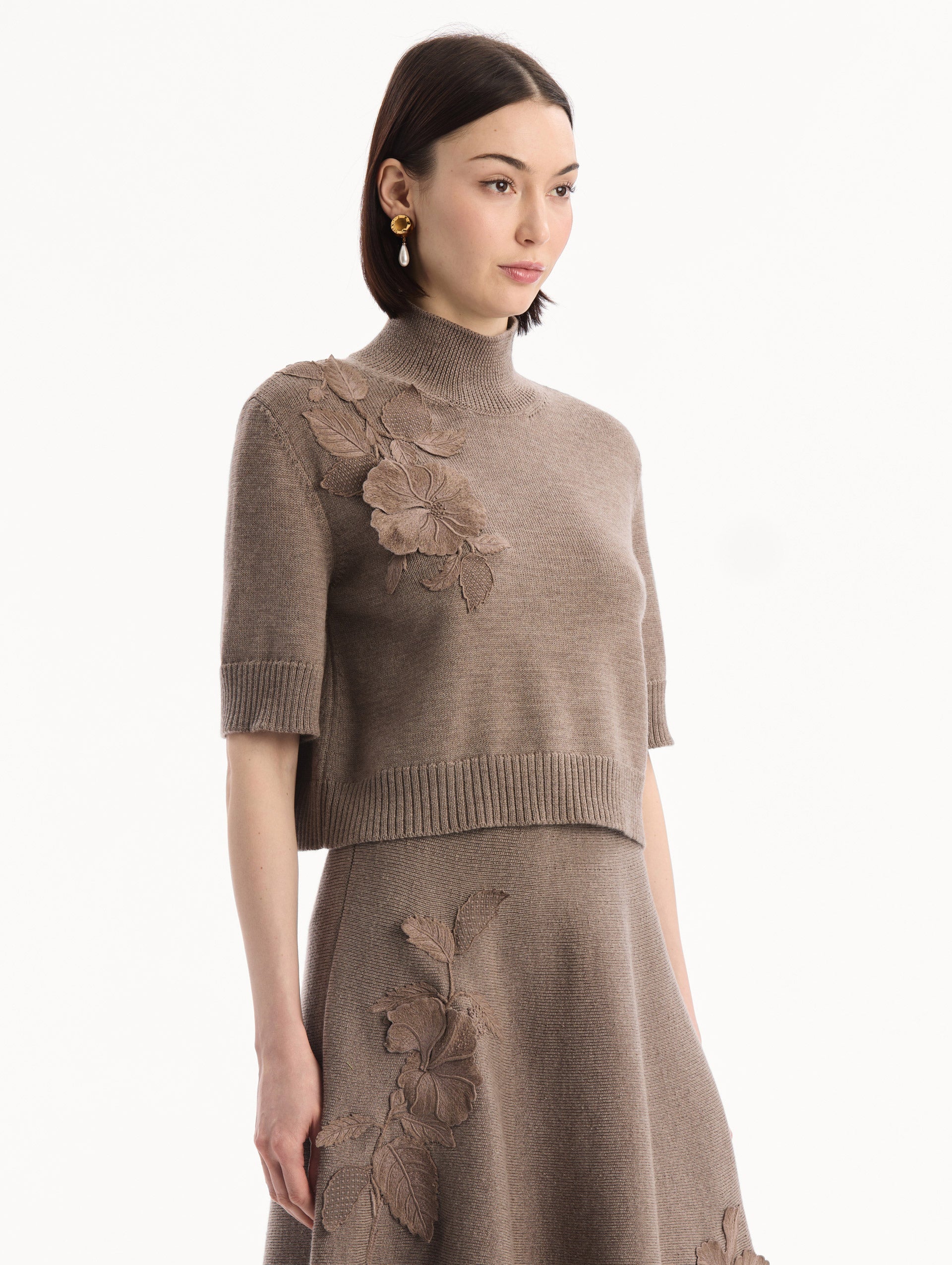 The model is wearing the Hibiscus Embroidered Knit Pullover. Featuring a high neckline and ribbed trim. Side View.