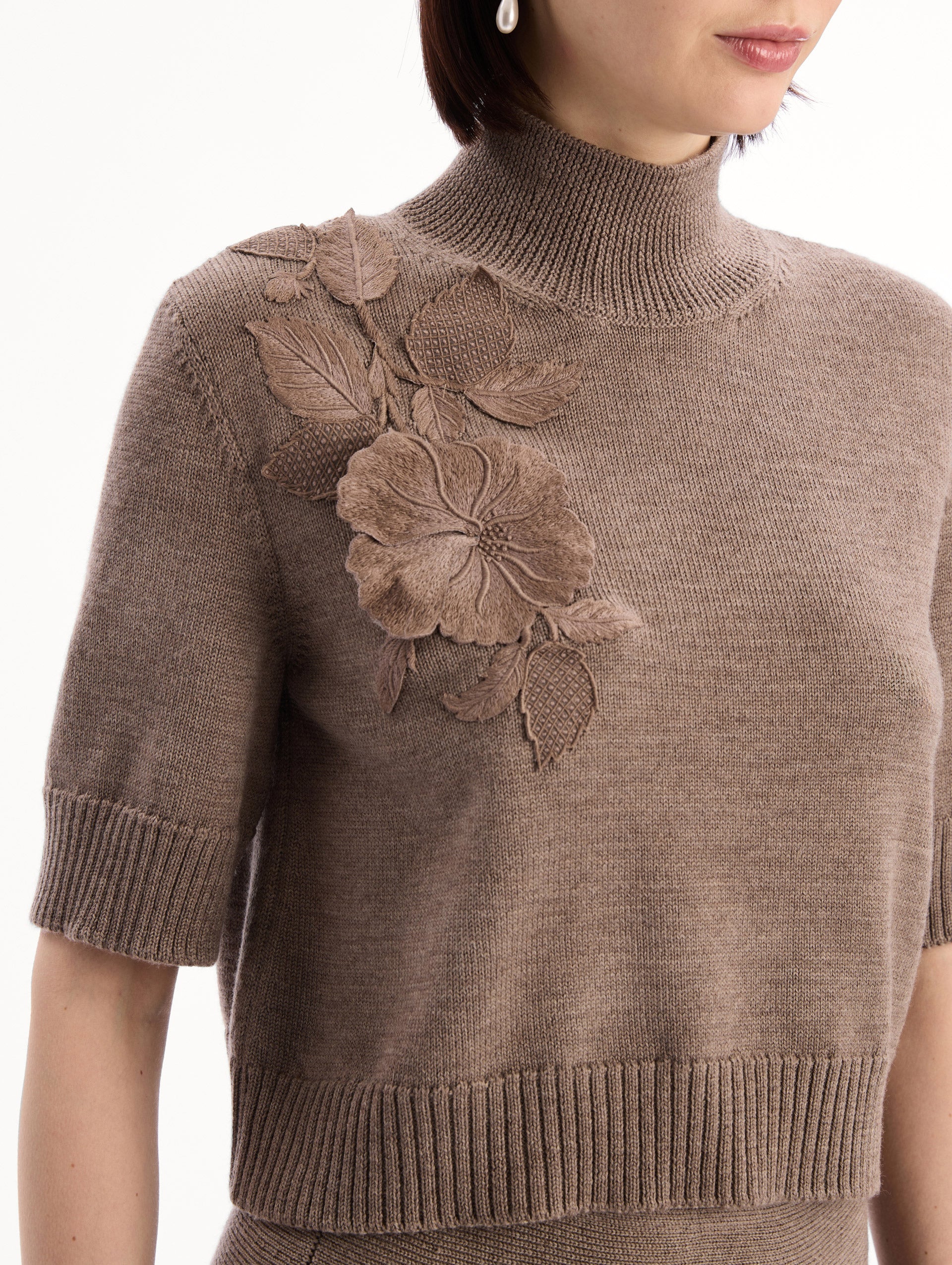 The model is wearing the Hibiscus Embroidered Knit Pullover. Featuring a high neckline and ribbed trim. Detail View.
