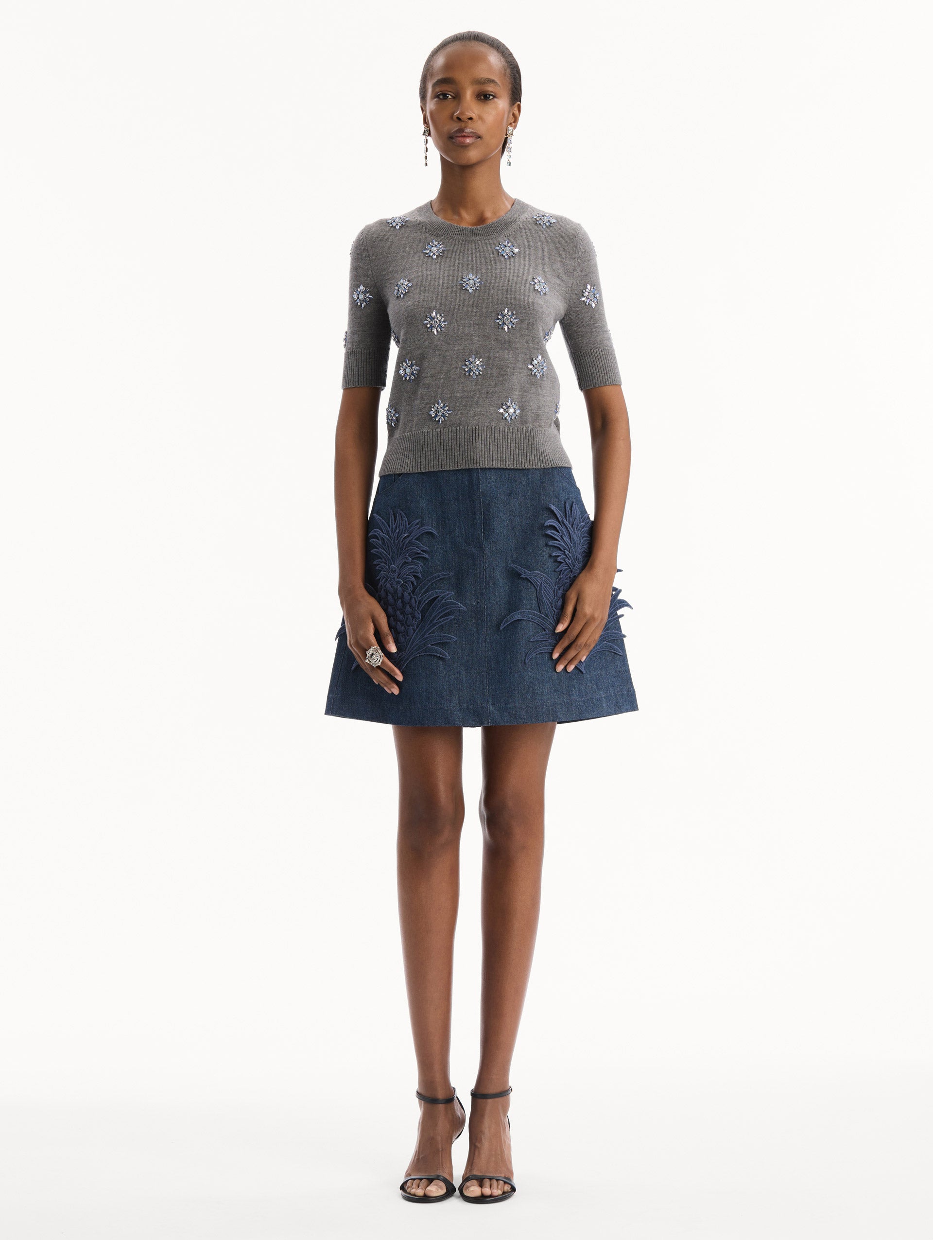 The model is wearing the Crystal Embroidered Pullover in grey with blue crystal embroidered. Featuring a crew neckline and ribbed trims. Front View.