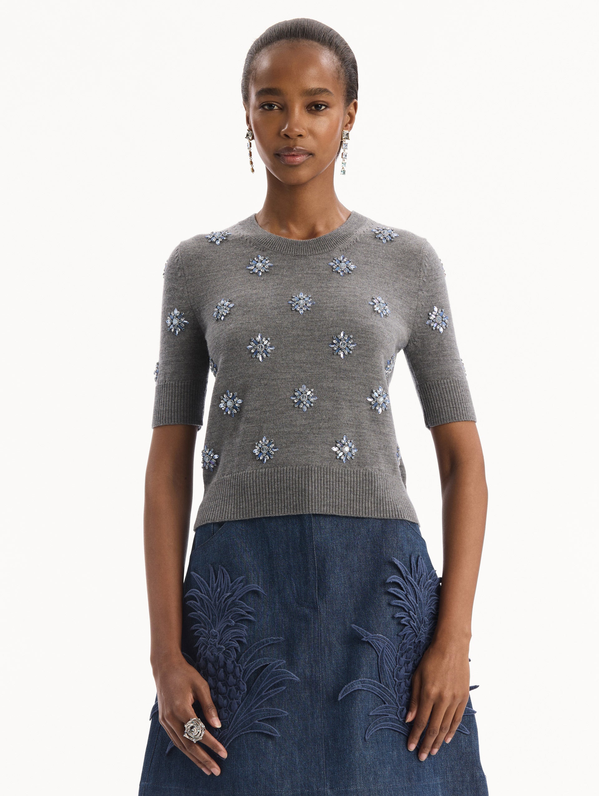 The model is wearing the Crystal Embroidered Pullover in grey with blue crystal embroidered. Featuring a crew neckline and ribbed trims. Front View.