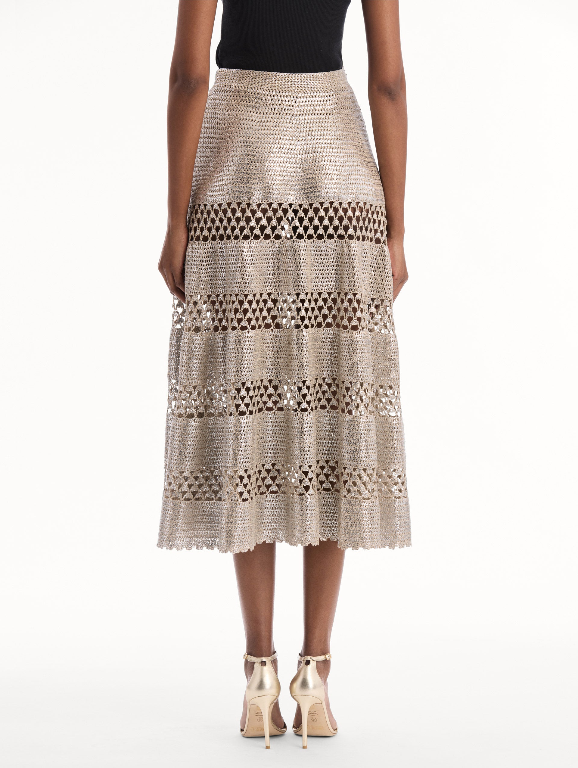 The model is wearing the Silver Foil Midi Skirt. Featuring a tiered silhouette with striped intricate openwork and midi length. Back View.
