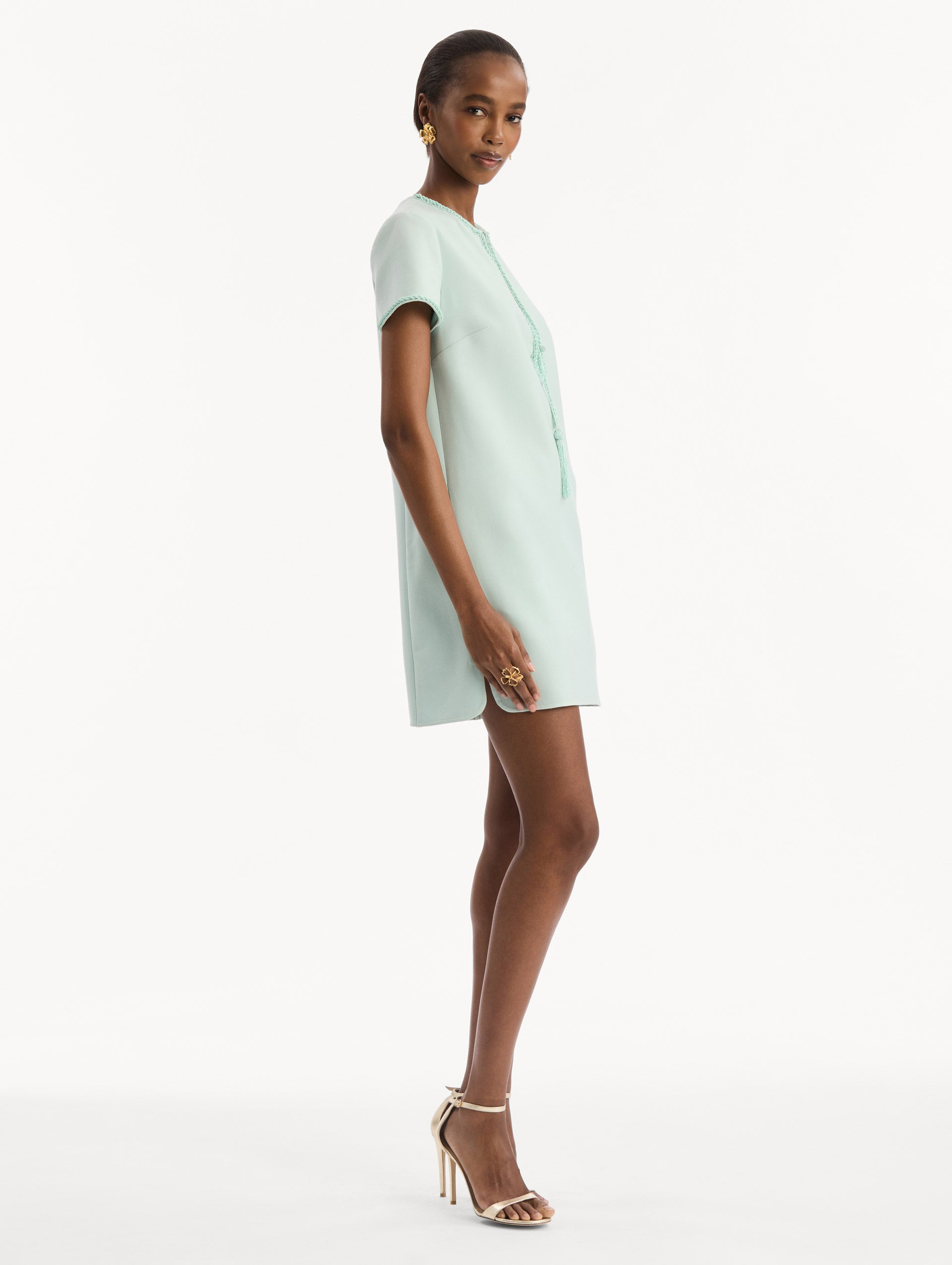 The model is wearing the Beaded Bow-Detail Shift Dress in Saltwater Blue. Featuring a beaded bow detail at the neckline with tassel ties and subtle trim along the edges. Side View.