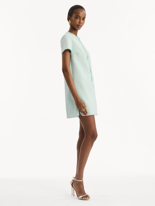The model is wearing the Beaded Bow-Detail Shift Dress in Saltwater Blue. Featuring a beaded bow detail at the neckline with tassel ties and subtle trim along the edges. Side View.