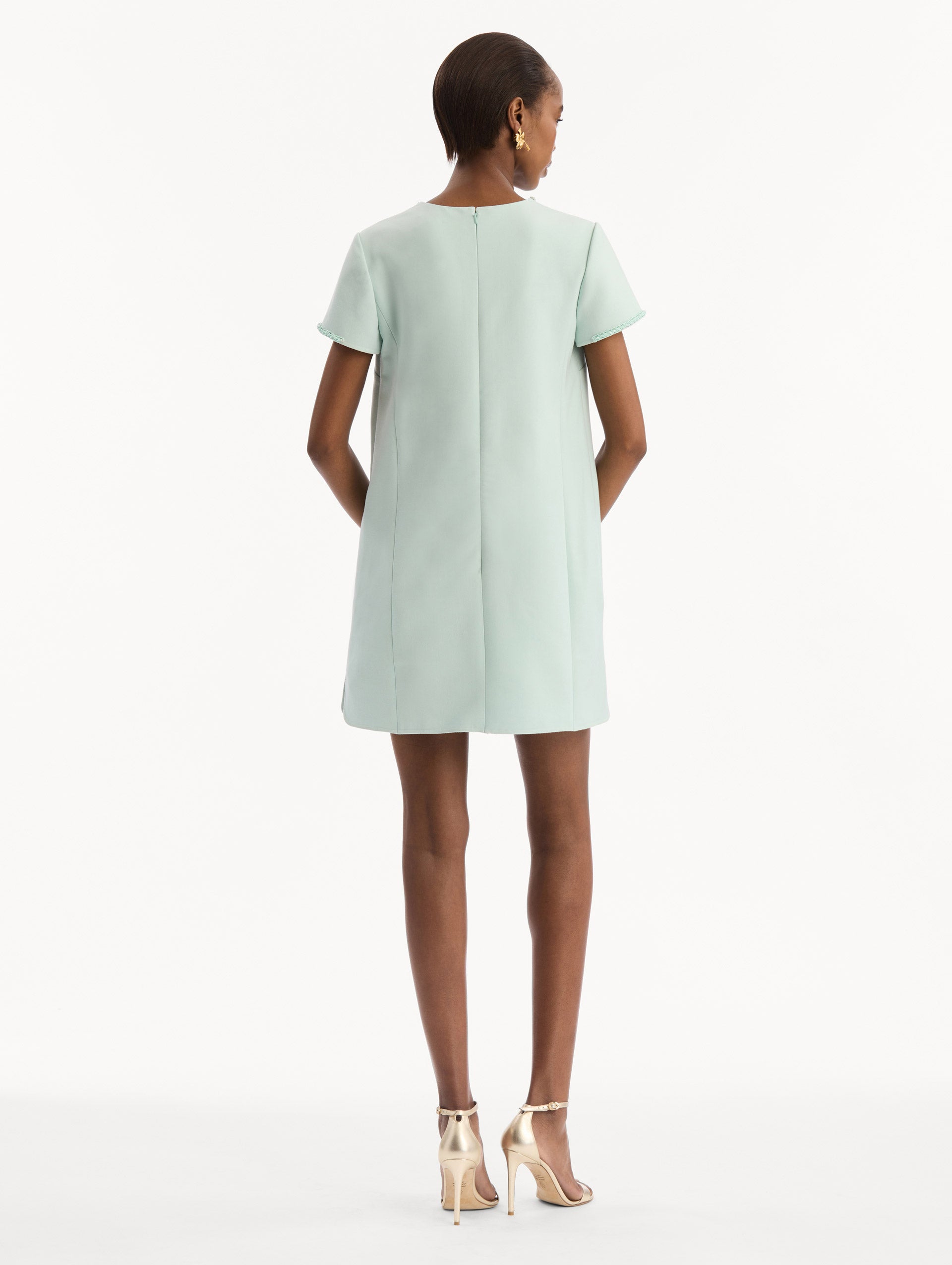 The model is wearing the Beaded Bow-Detail Shift Dress in Saltwater Blue. Featuring a beaded bow detail at the neckline with tassel ties and subtle trim along the edges. Back View.